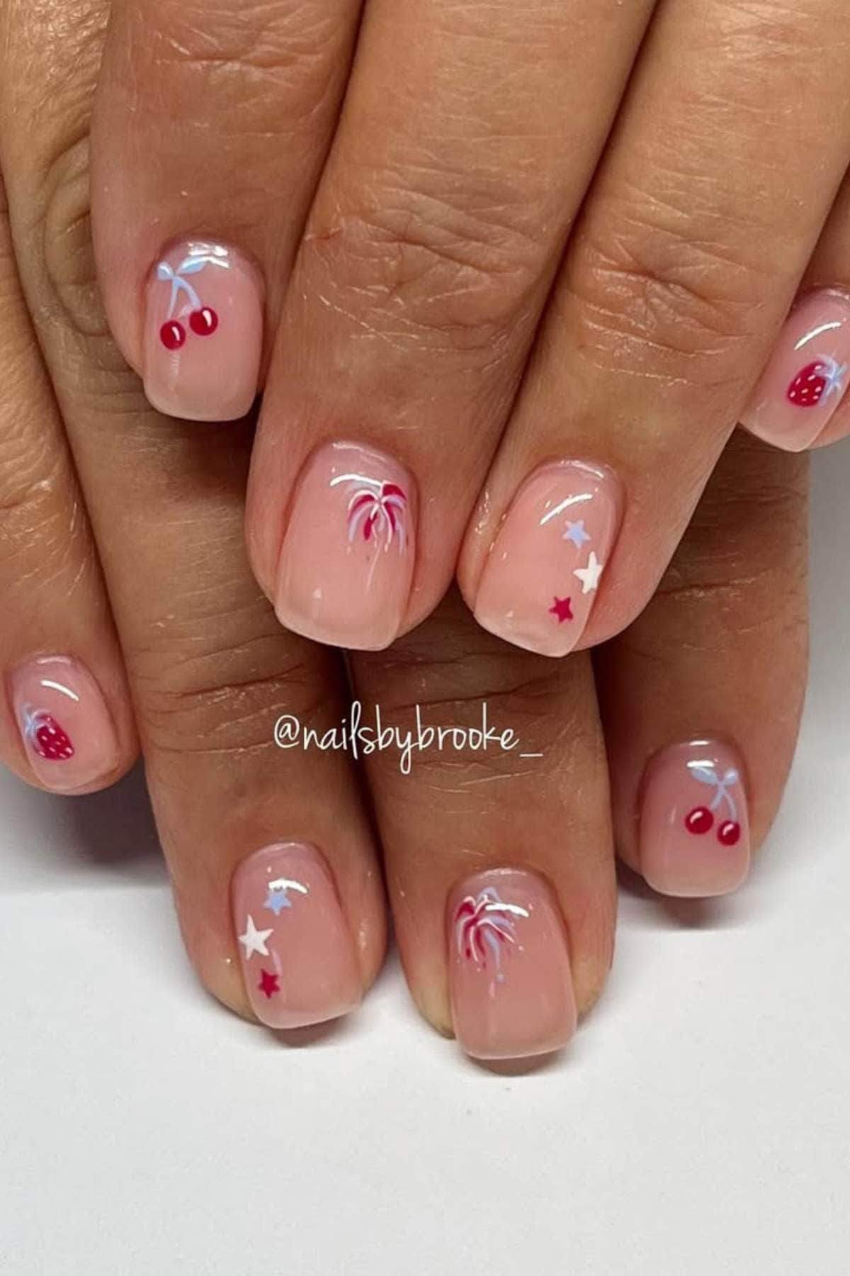 Nails with a sheer pink polish featuring red and white cherries, strawberries, palm trees, and stars.