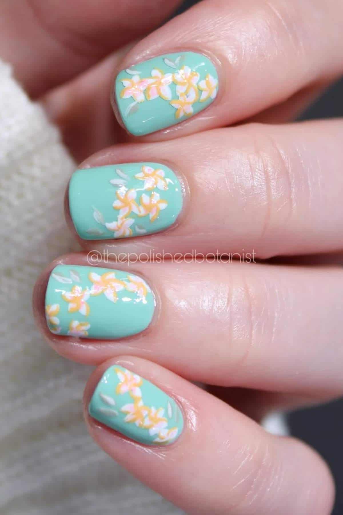 A hand with short nails painted light turquoise, featuring small yellow and white floral designs on each nail.