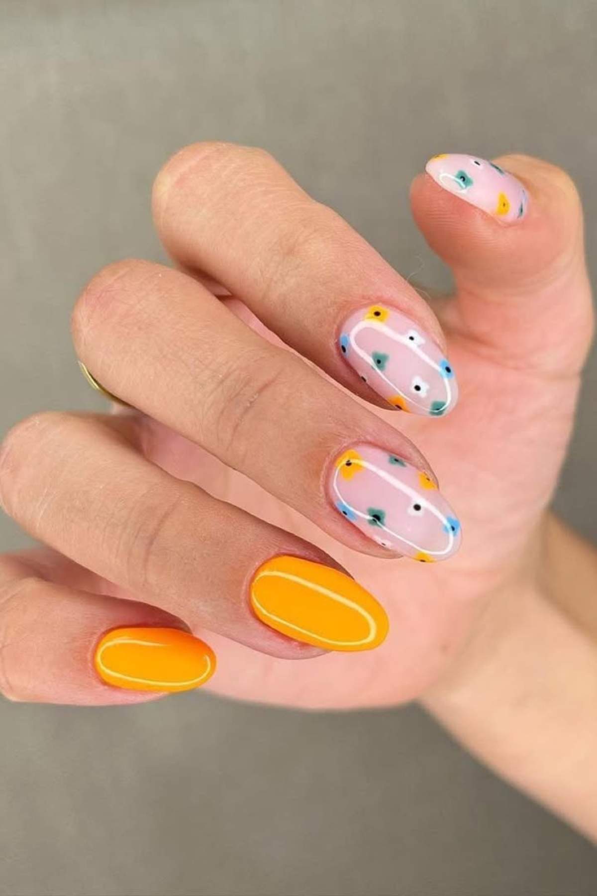 A hand with manicured nails featuring a mix of solid orange and pastel pink with abstract colorful dot and line designs.