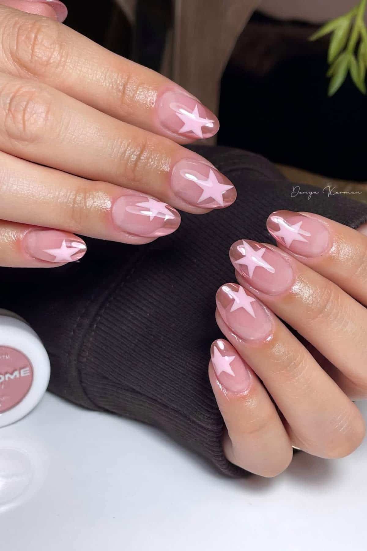 Hands with almond-shaped nails painted light pink, each nail decorated with white star designs.