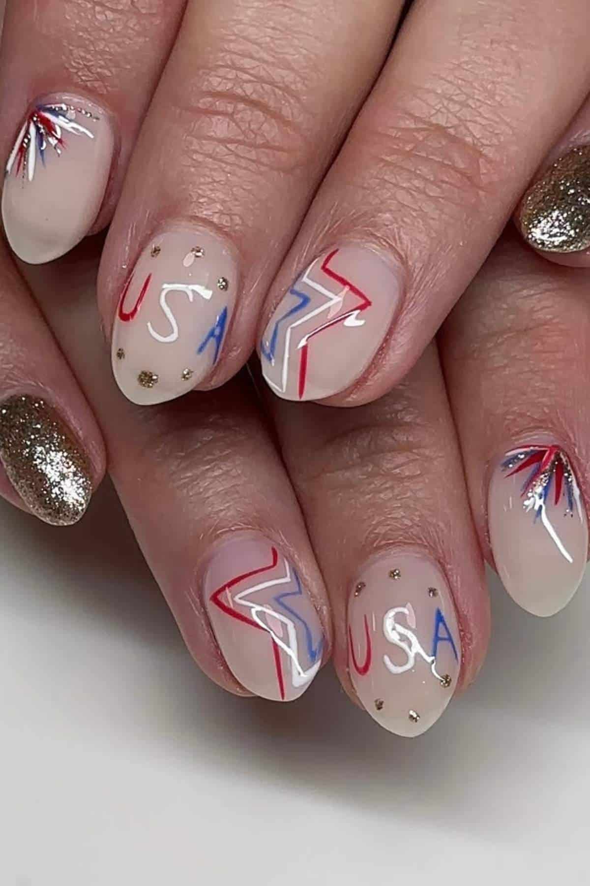 Nails with a sheer nude polish featuring red, white, and blue patriotic designs, including "USA" text, lightning bolts, and abstract bursts, plus two gold glitter accent nails.