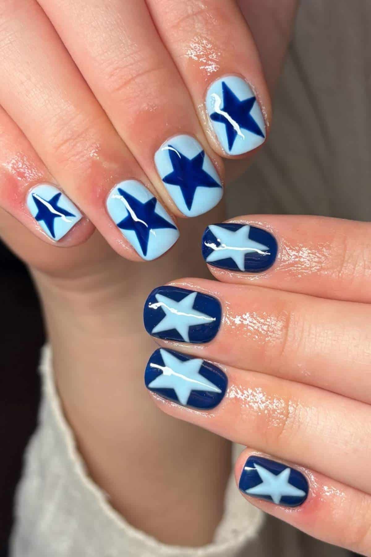 Hands with manicured nails featuring large blue and white star designs on a light blue and dark blue background.