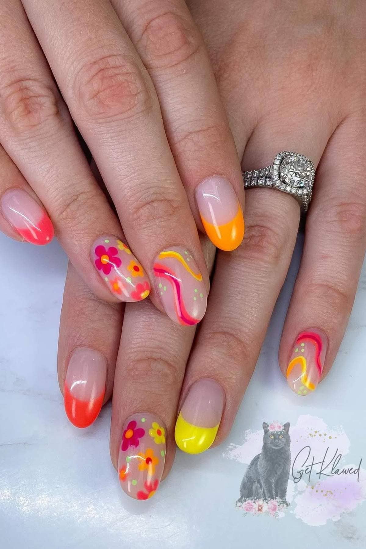 Hands with long almond-shaped nails featuring colorful designs, including neon French tips, flowers, and swirls in pink, yellow, and orange. Person wears a diamond engagement ring.