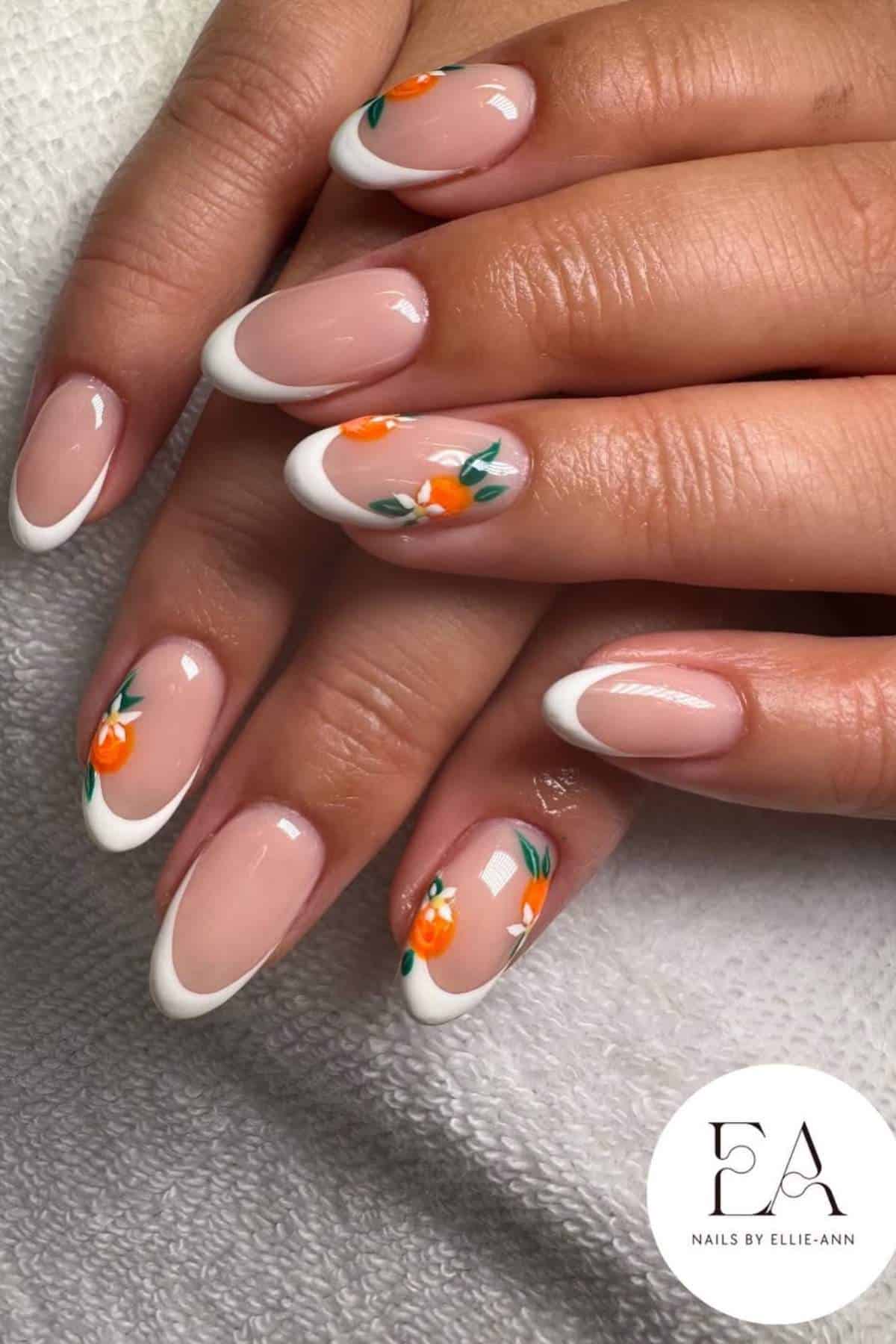 Close-up of manicured hands with long, almond-shaped nails featuring white French tips and small orange fruit designs on a few nails.
