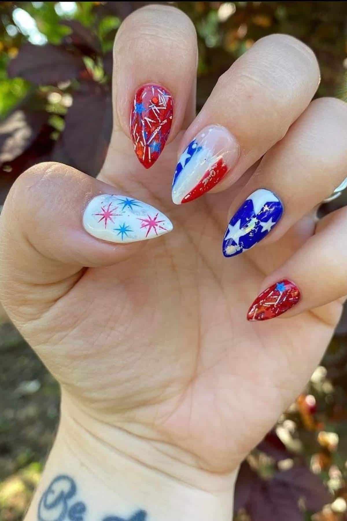 Close-up of a hand with red, white, and blue stiletto nails decorated with stars and glitter.