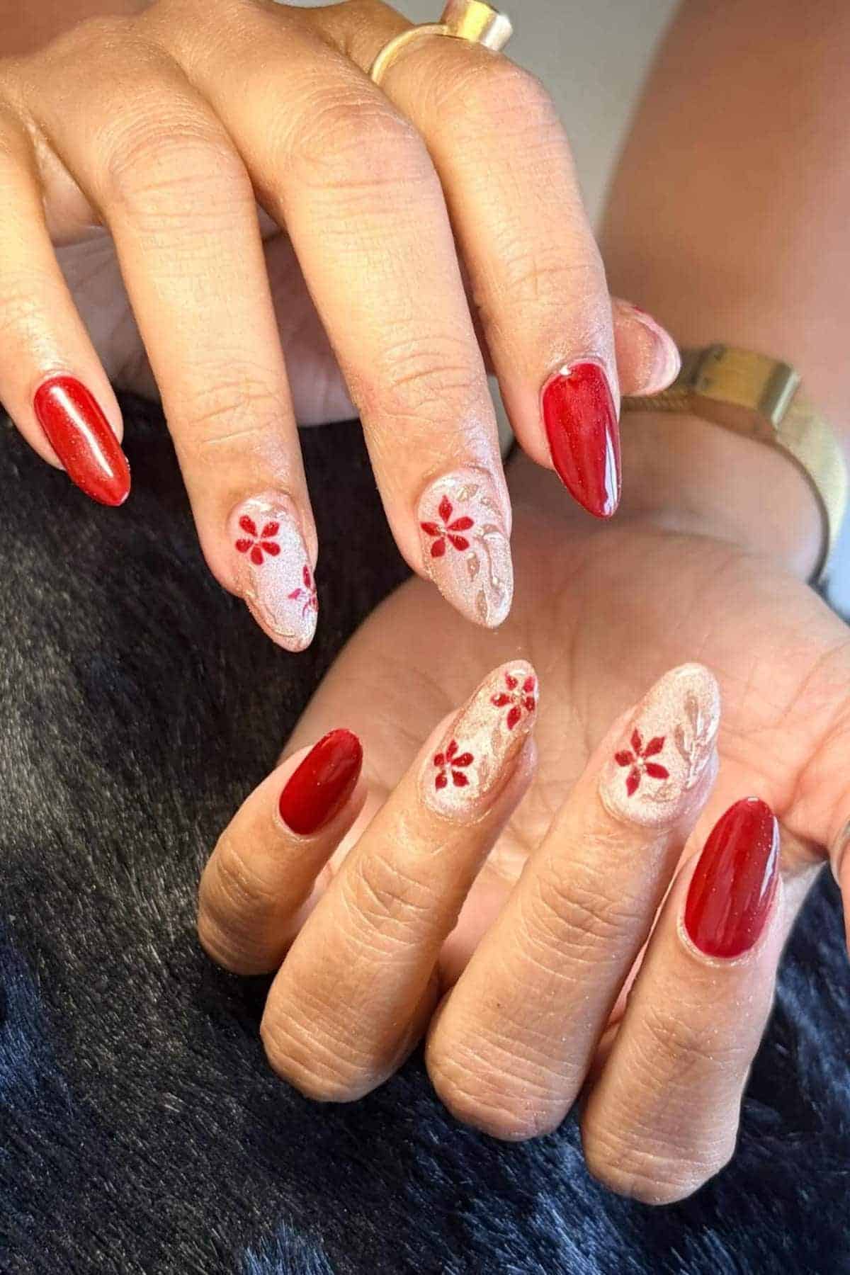 Hands with almond-shaped nails; some nails are painted red, others nude with red floral designs and white accents.
