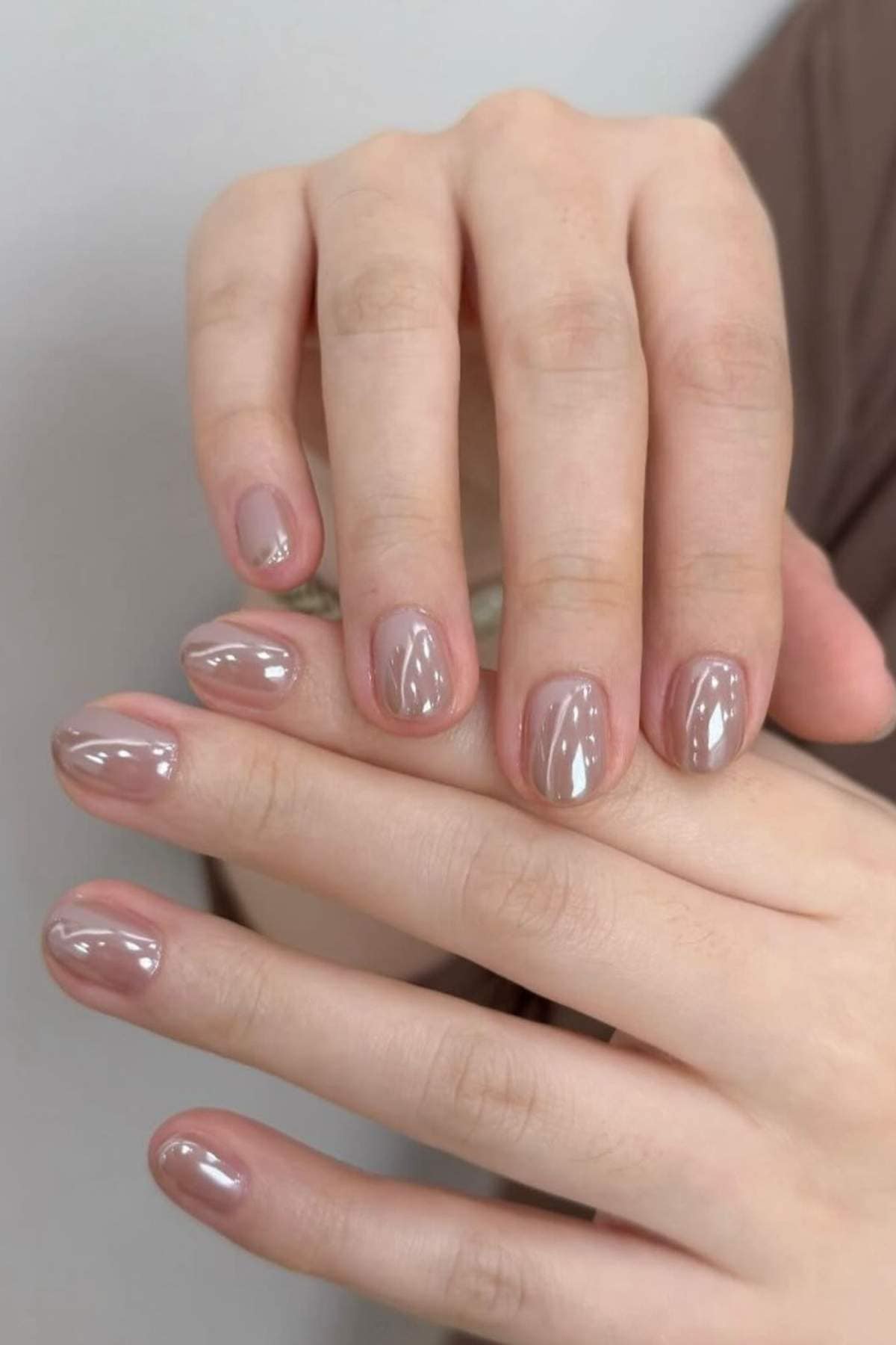Close-up of hands with short, neatly manicured nails painted in a glossy nude beige color.