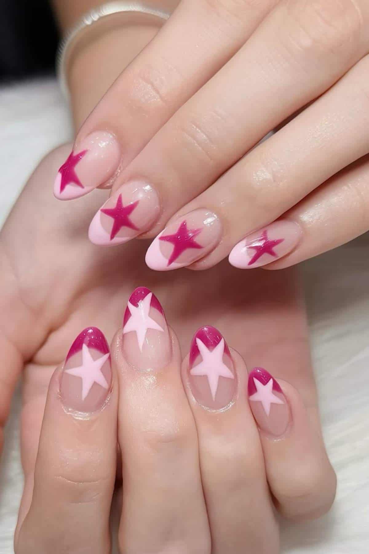 Hands with almond-shaped nails featuring pink and magenta star designs on a pale pink base.