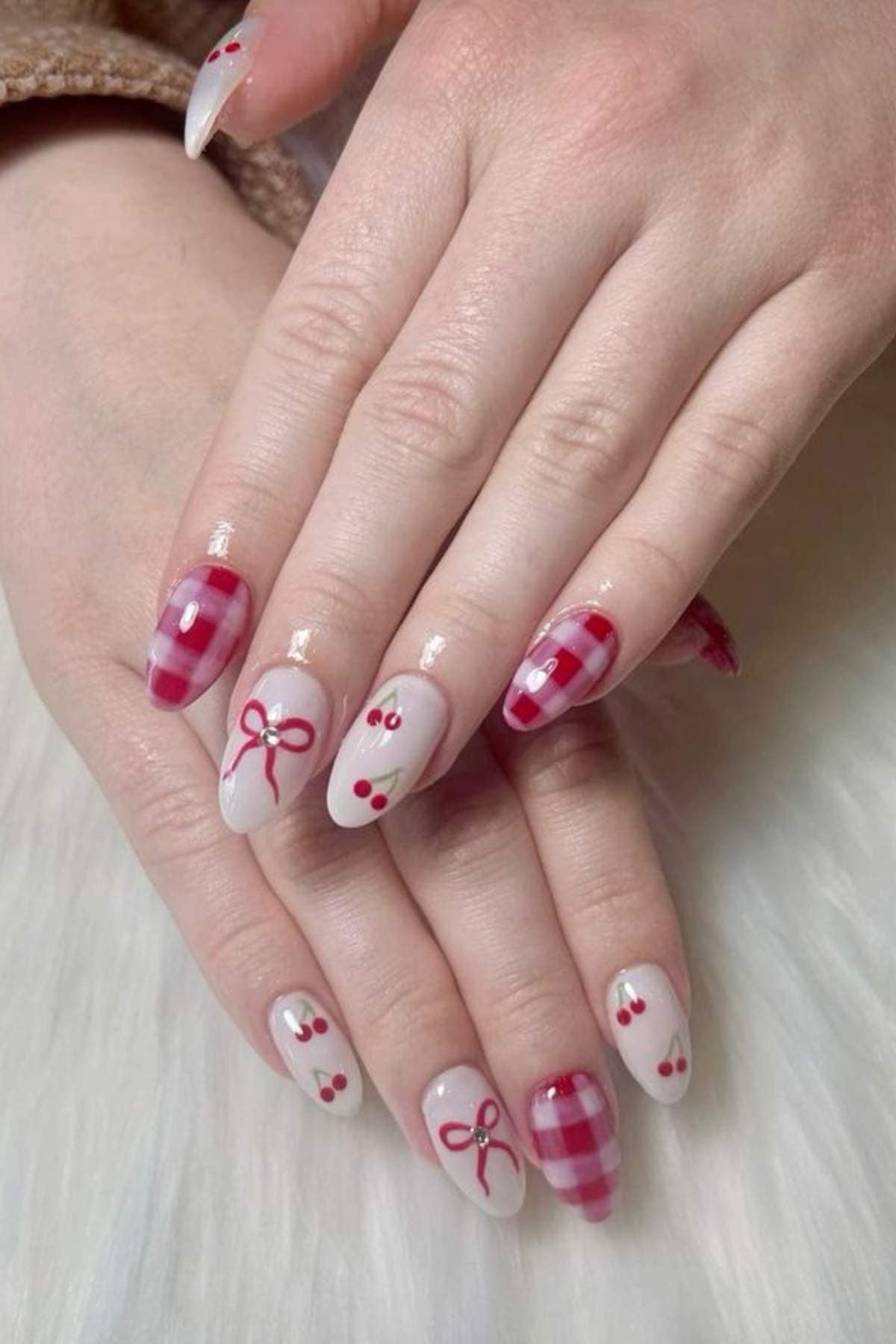 Hands with long nails featuring a pink and white plaid pattern, red bows, and small red cherry designs on a white background.