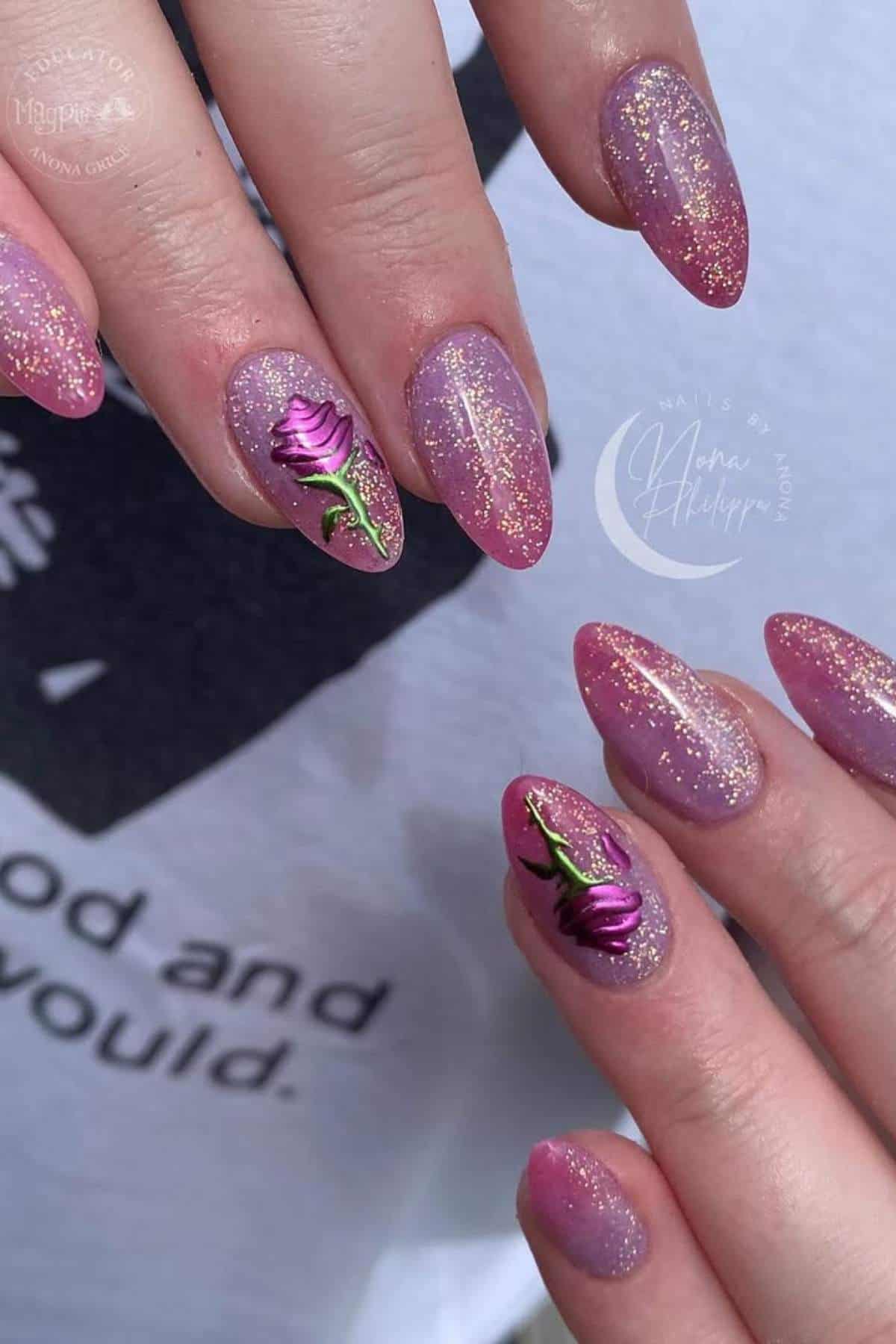 Close-up of a hand with almond-shaped nails painted in shimmery pink and gold polish, featuring purple rose nail art on two accent nails.