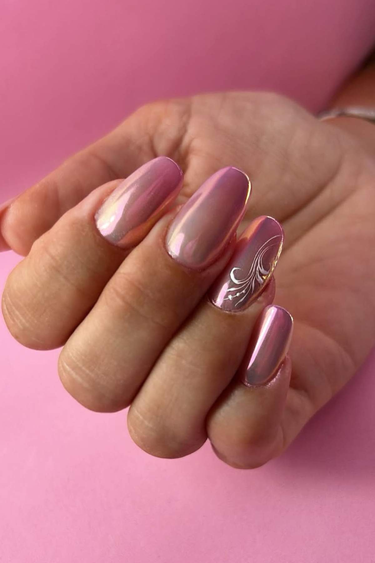 A hand with shiny, light pink manicured nails; the ring finger features a white decorative swirl design.
