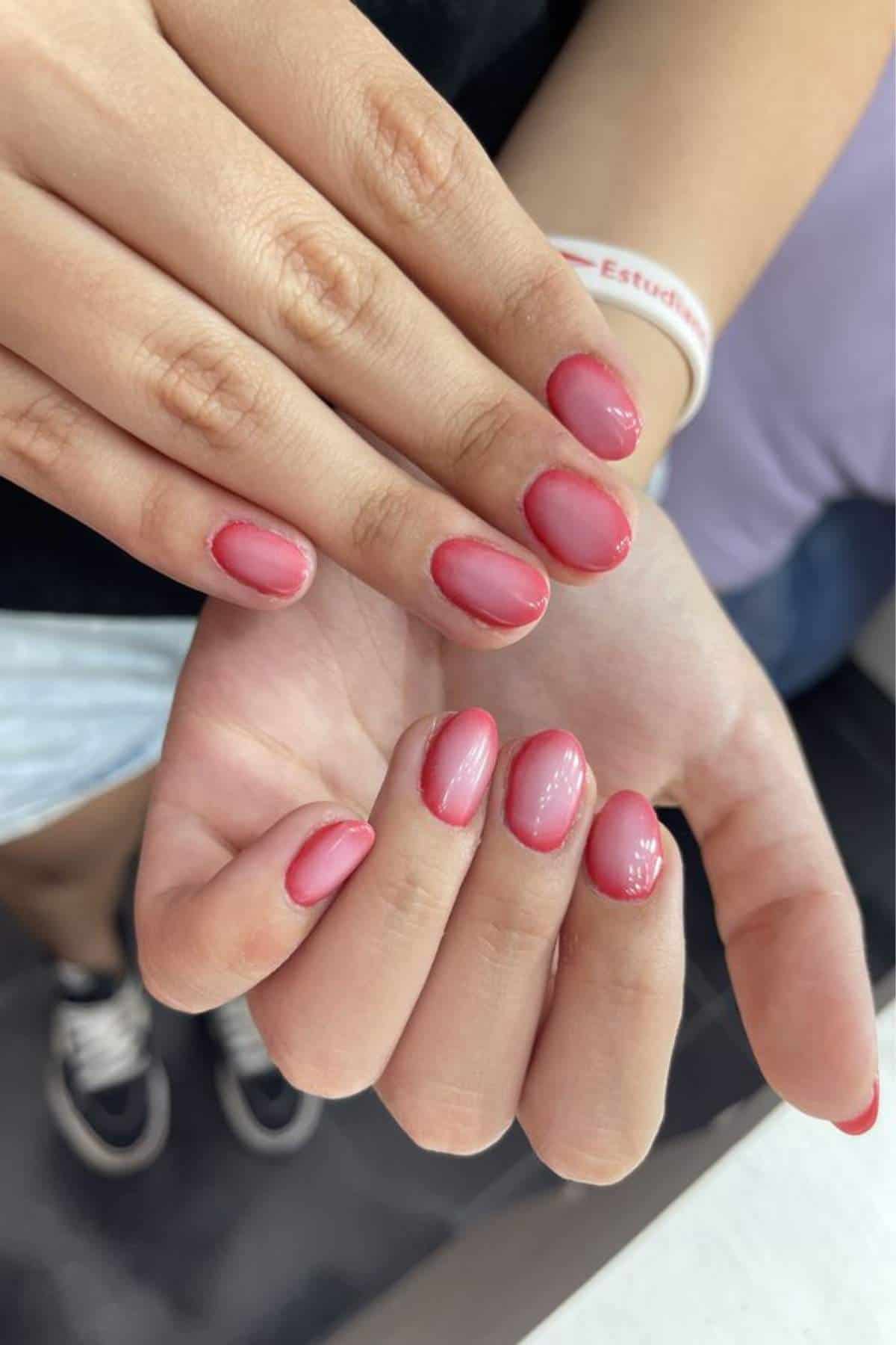 Close-up of hands showing fingernails painted with a glossy pink polish and natural half-moon design near the cuticles.