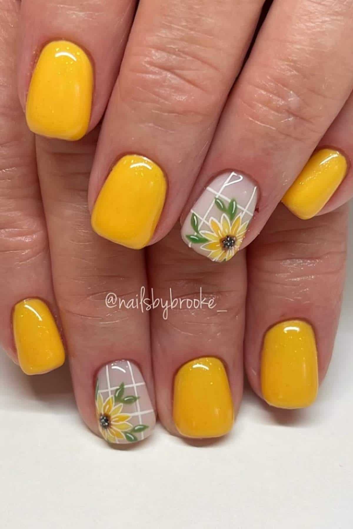 Hands with yellow nail polish; two accent nails feature sunflower designs and white grid lines.