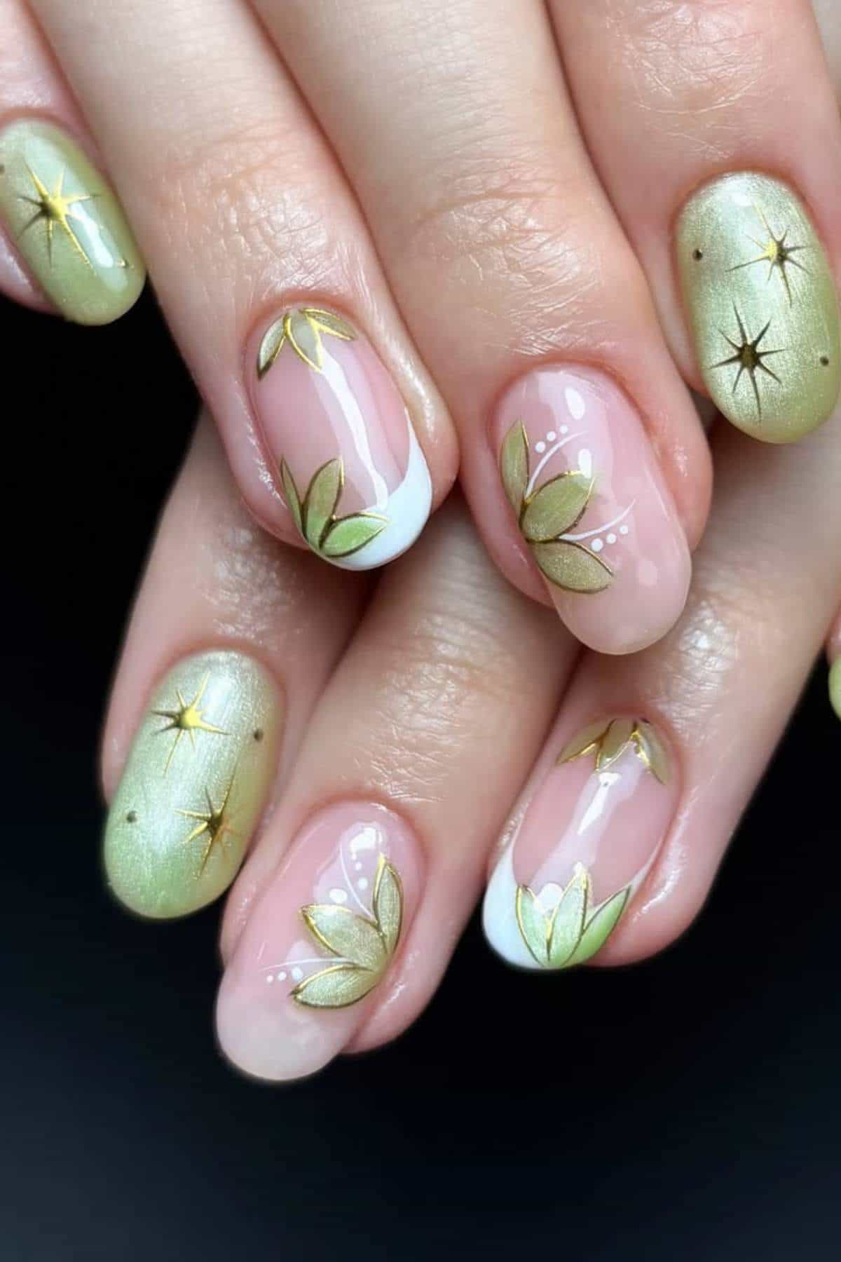 Close-up of hands with manicured nails featuring green polish, gold star designs, and delicate floral patterns on a black background.
