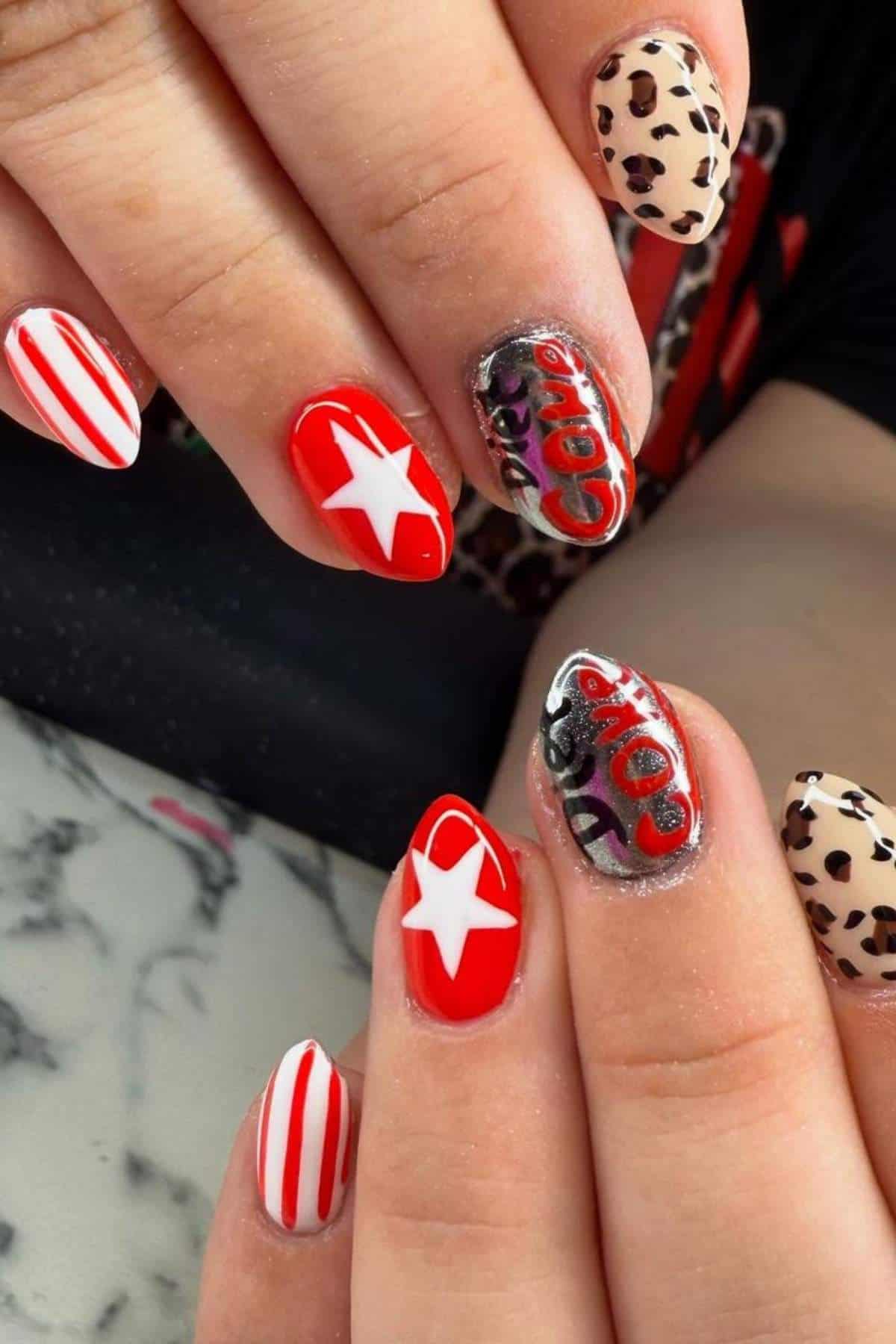 A hand with red and white Coca-Cola themed nail art, including stars, stripes, lettering, and leopard print designs on some nails.