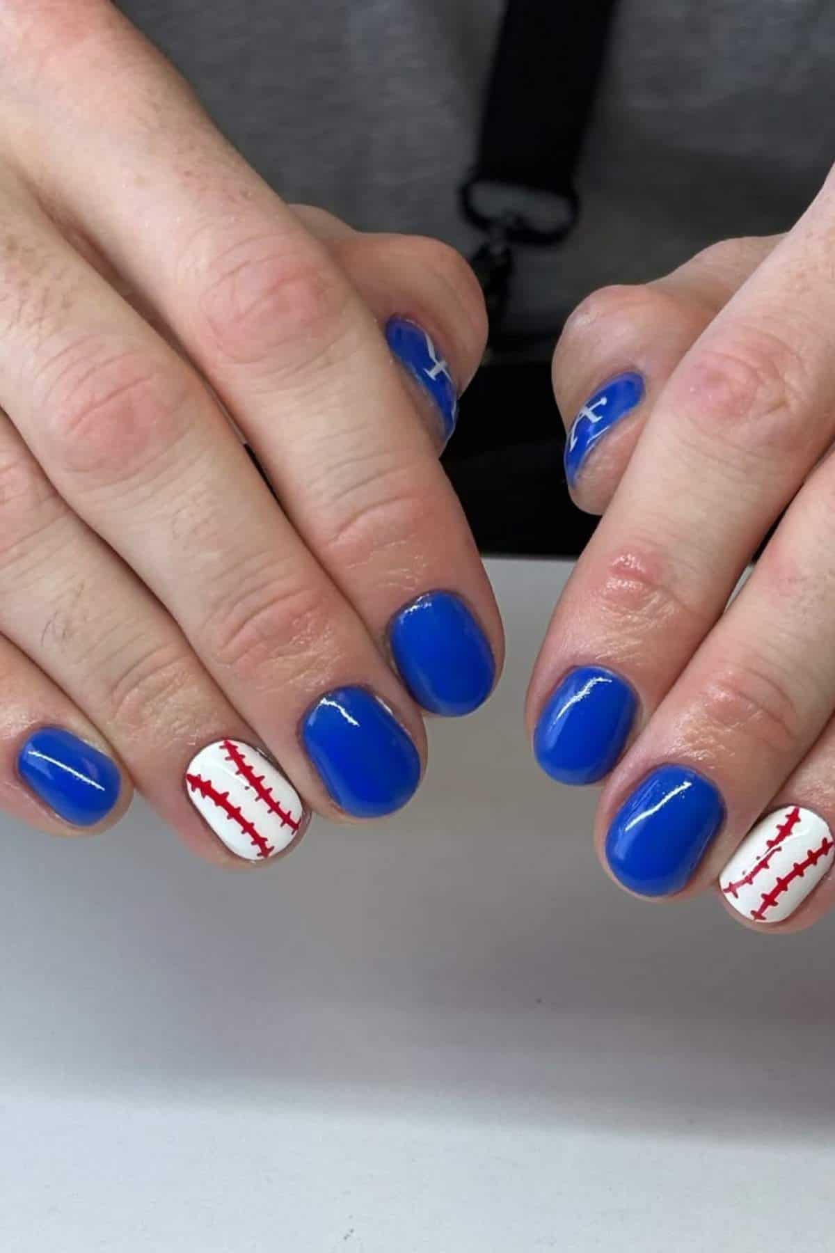 Hands with short nails painted blue, except for two nails on each hand, which are painted white with red stitching resembling a baseball design.