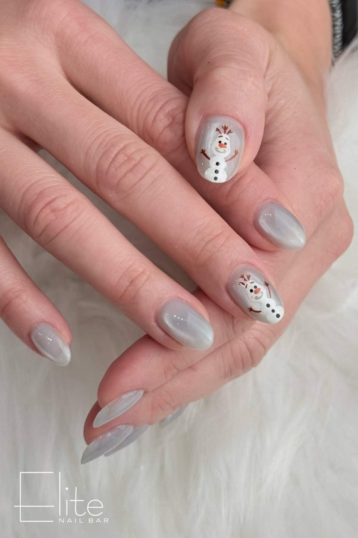 Hands with light gray manicured nails; two nails feature a snowman design. The image has the "Elite Nail Bar" logo in the corner.