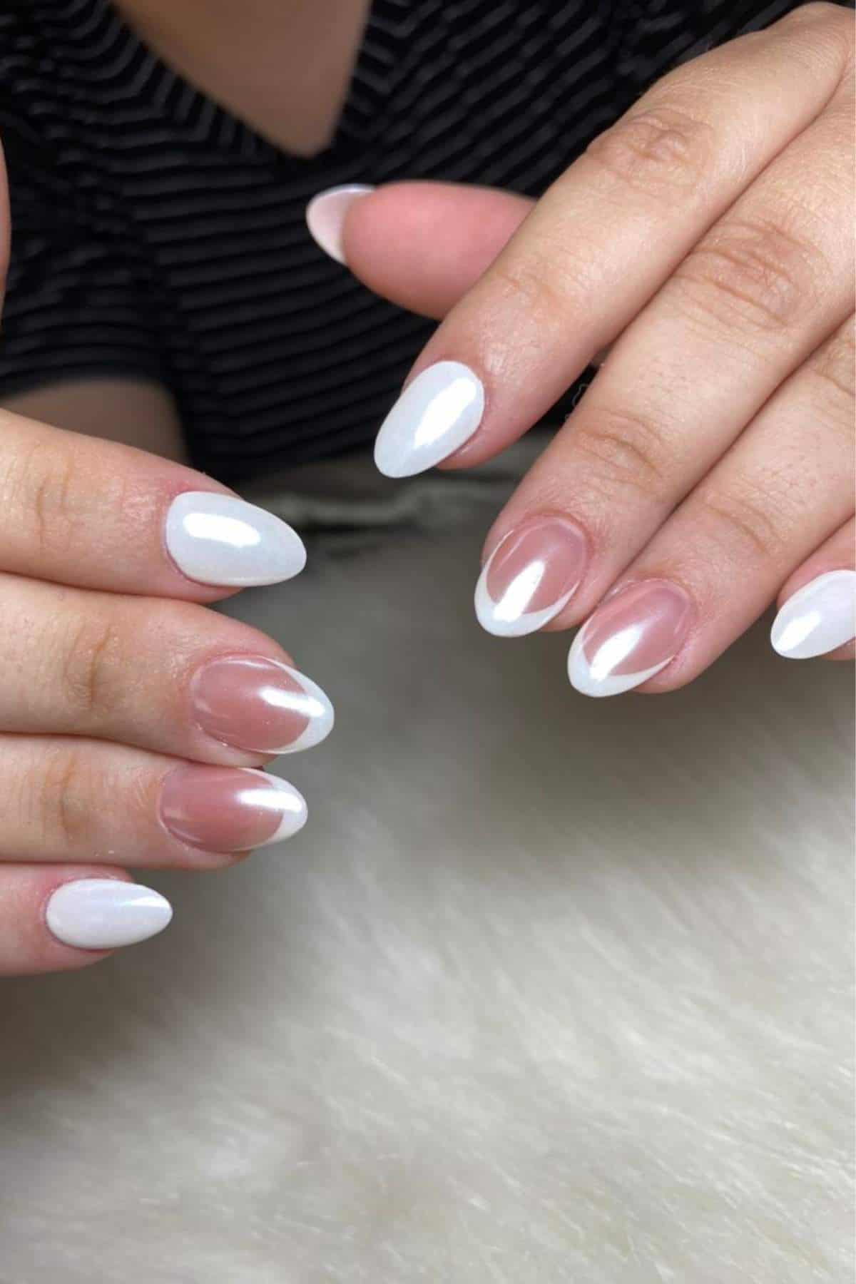 Hands with almond-shaped nails; some nails are painted solid white, while others have a white French tip design on a natural base.
