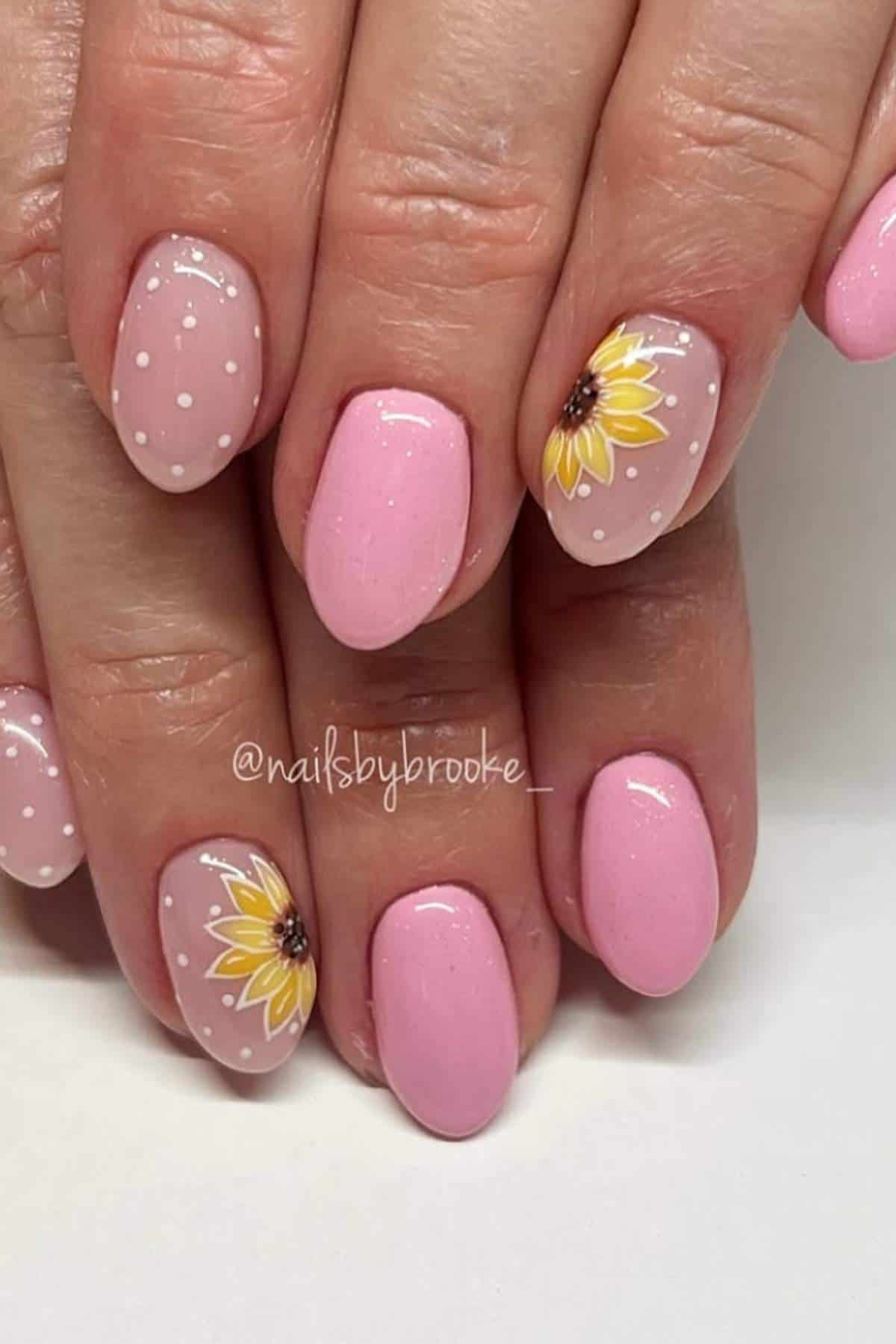 Hands with oval-shaped nails painted light pink; some nails feature white polka dots or sunflower designs on a nude base.