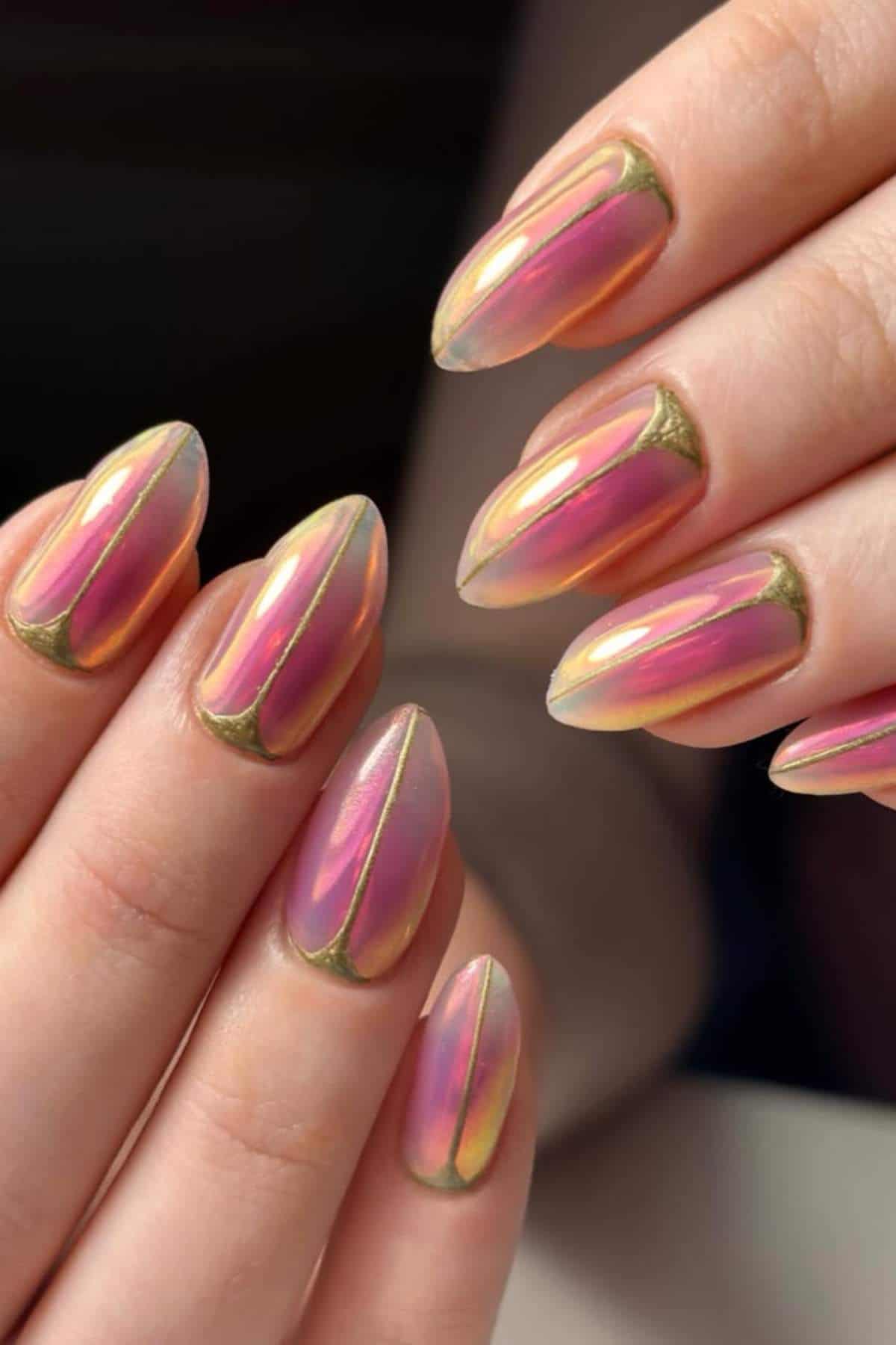 Close-up of hands with almond-shaped nails featuring a shiny, iridescent pink finish and gold accents near the cuticles.