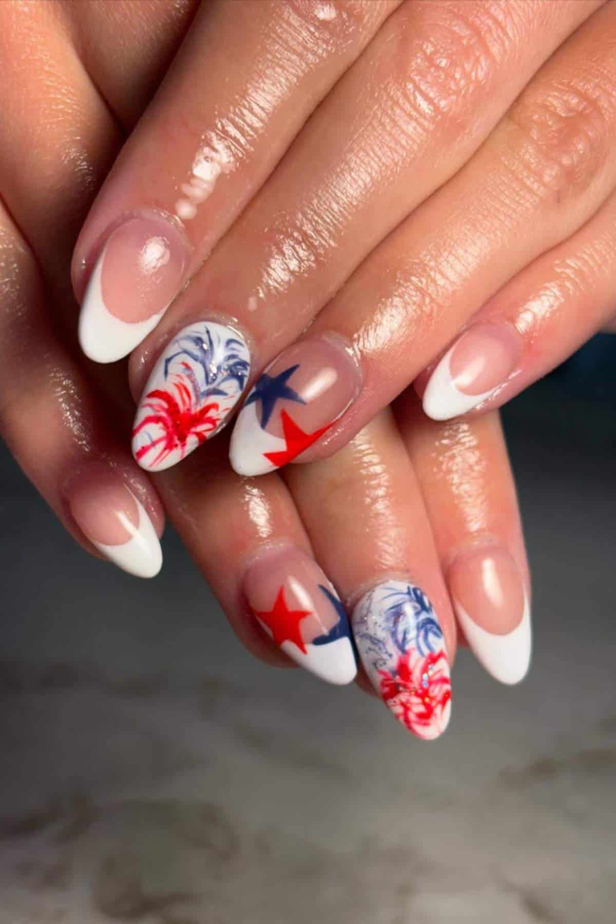 French tip nails with red, white, and blue patriotic designs, including stars and abstract swirls.