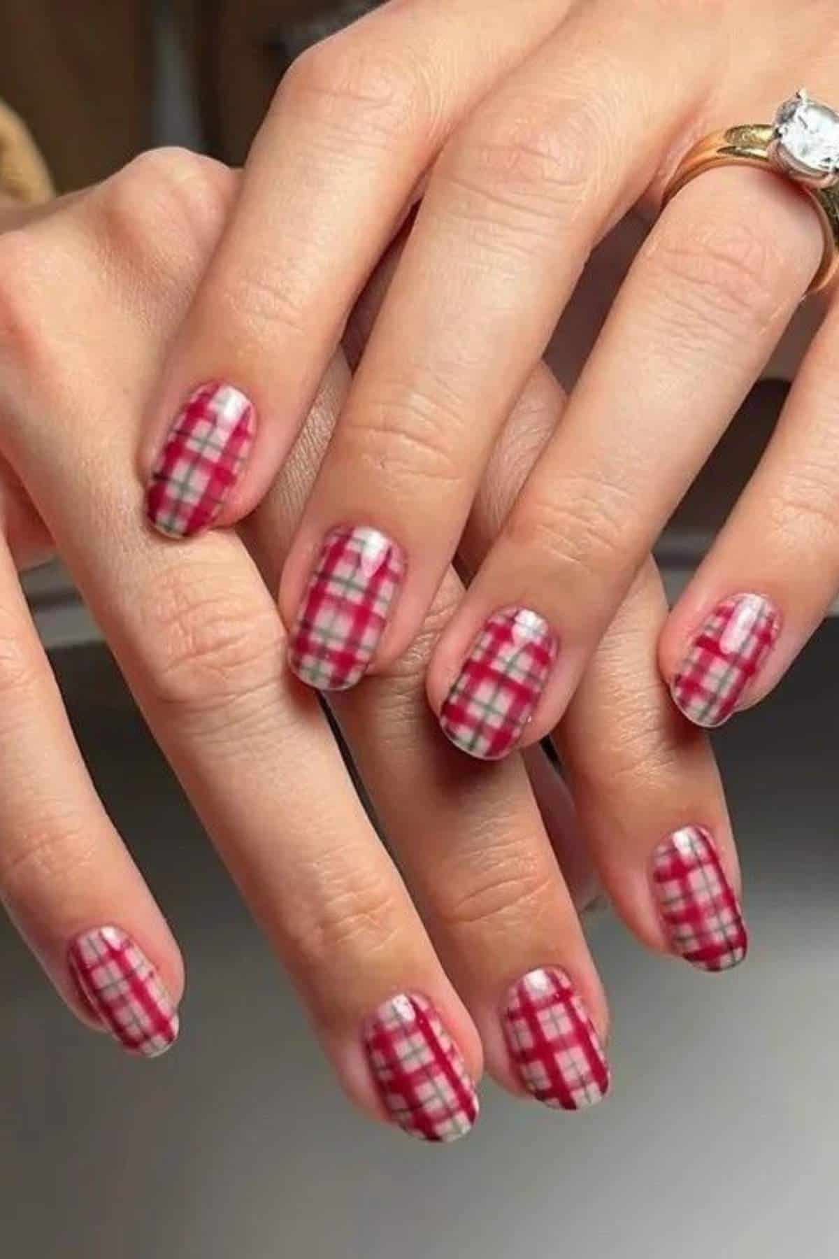 Hands with neatly manicured nails featuring a red and white plaid pattern; one hand has a gold ring with a large clear gemstone.