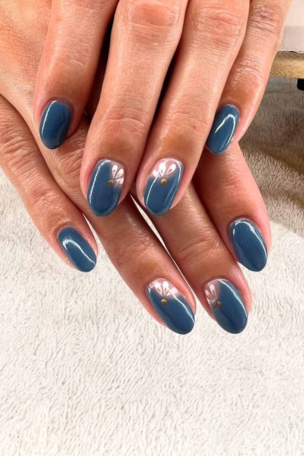Hands with short, oval-shaped nails painted blue; accent nails feature a white daisy design with a yellow center near the cuticle.