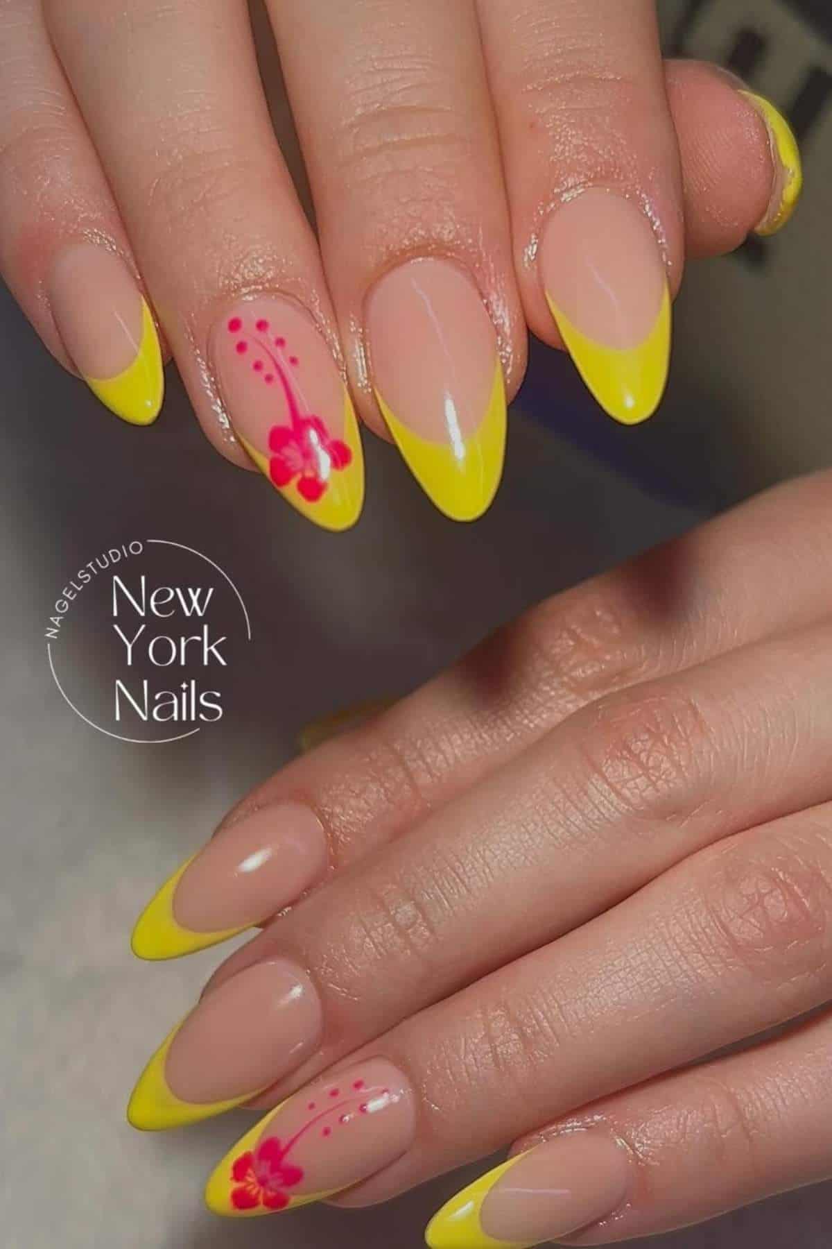 Hands with almond-shaped nails featuring yellow French tips and a pink floral design on two accent nails.