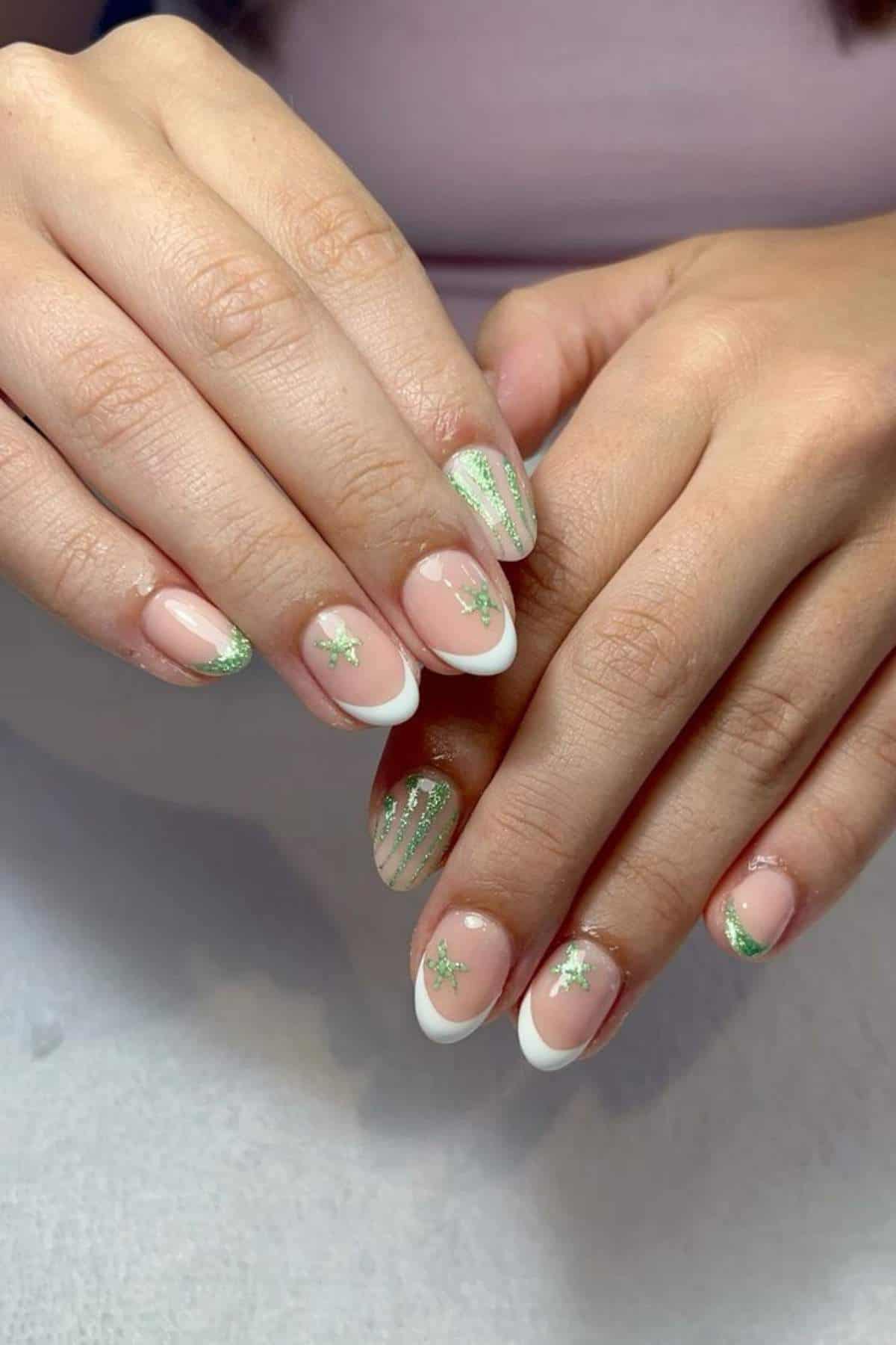 Hands with manicured nails featuring French tips, green glitter stars on most nails, and green glitter stripes on one accent nail.