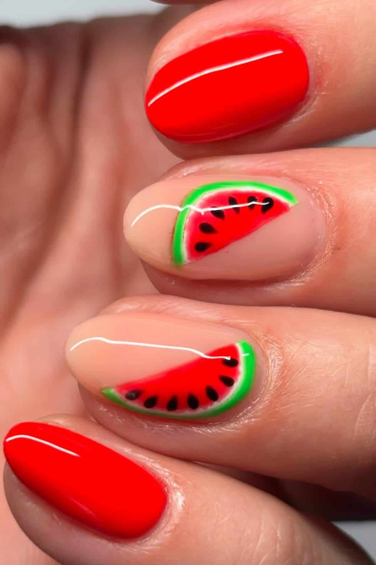 Close-up of a hand with red nail polish and two accent nails featuring watermelon slice nail art with green, red, and black detailing.