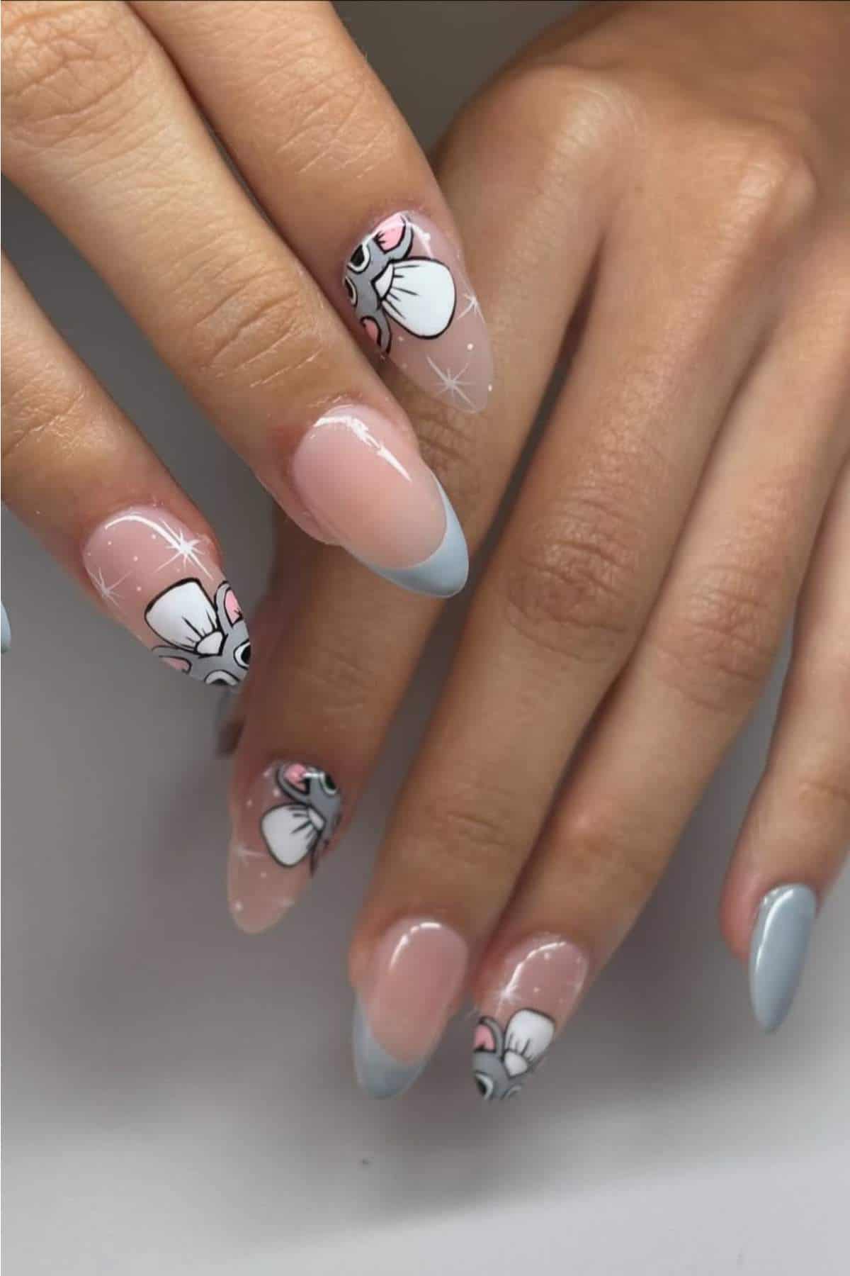Hands with almond-shaped nails, featuring blue French tips and cartoon mouse face nail art on two accent nails.