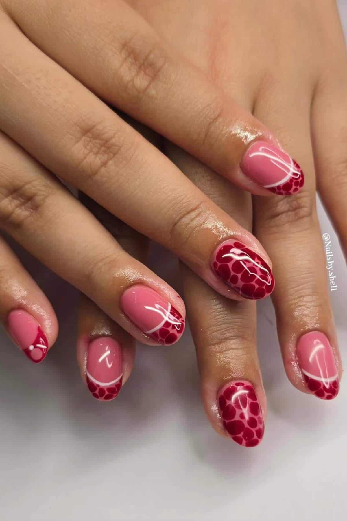 Close-up of hands with manicured nails featuring pink polish and red animal print patterns, with glossy finish and almond shape.