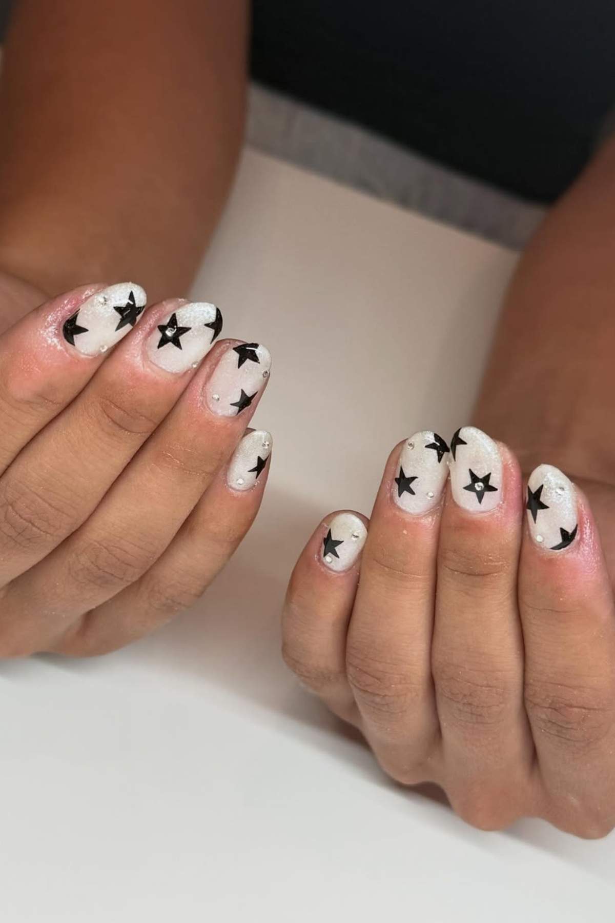 Hands with short, oval-shaped nails painted white and decorated with black star designs.