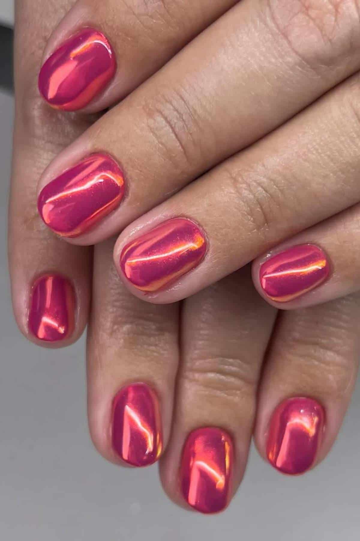 Close-up of hands with short, neatly manicured nails painted in a shiny, iridescent pink polish.