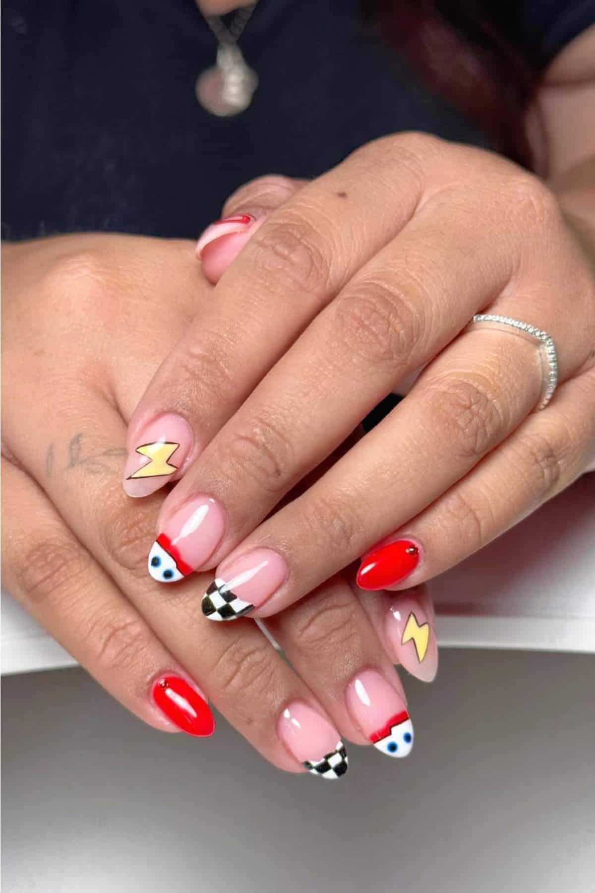 Hands with almond-shaped nails featuring a racing theme: red polish, black and white checkered pattern, yellow lightning bolts, and small blue and white dots.