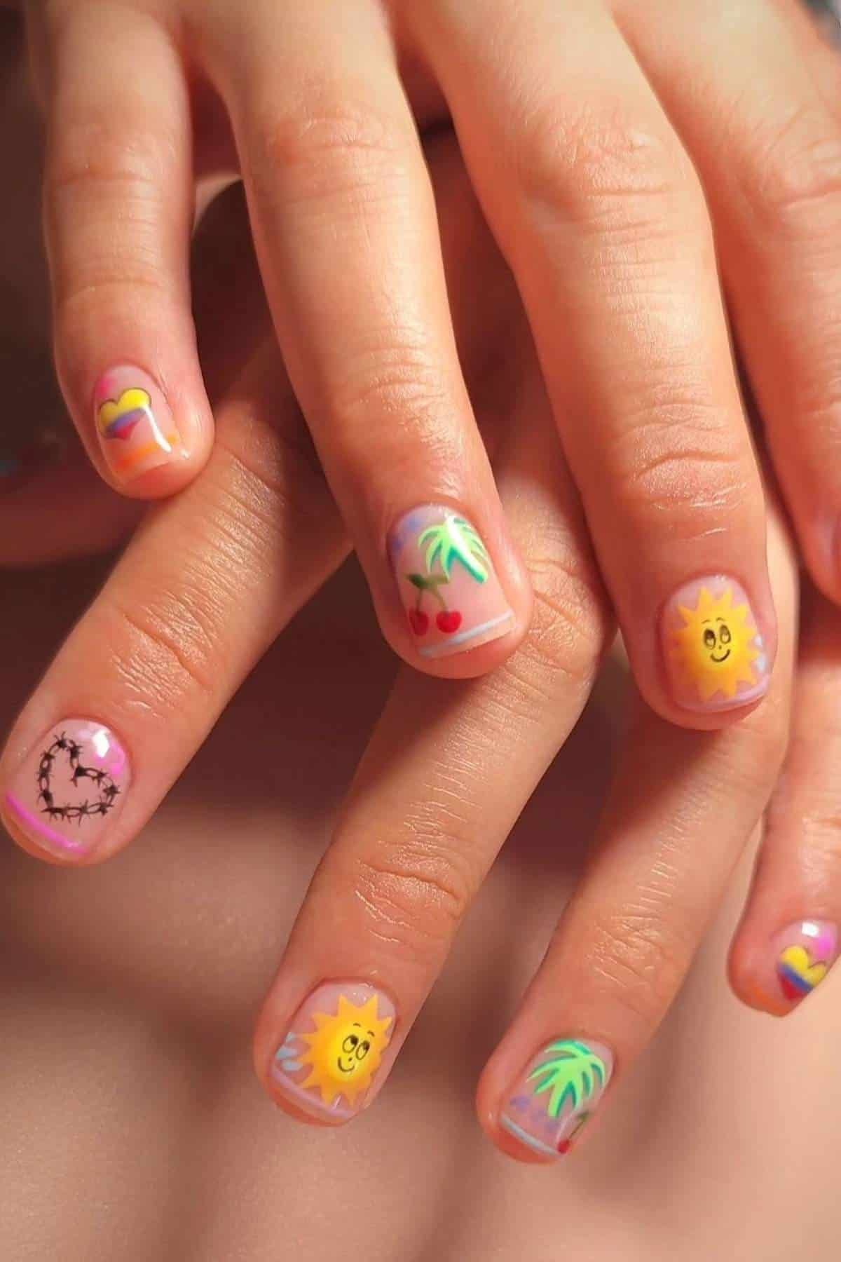 A close-up of hands with fingernails painted with colorful designs, including suns, palm trees, cherries, hearts, and barbed wire on a pastel background.
