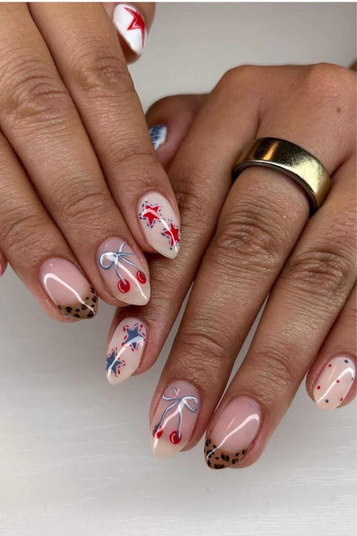 Hands with manicured nails featuring various designs, including cherries, bows, animal print tips, red and blue stars, and polka dots, against a plain white background.