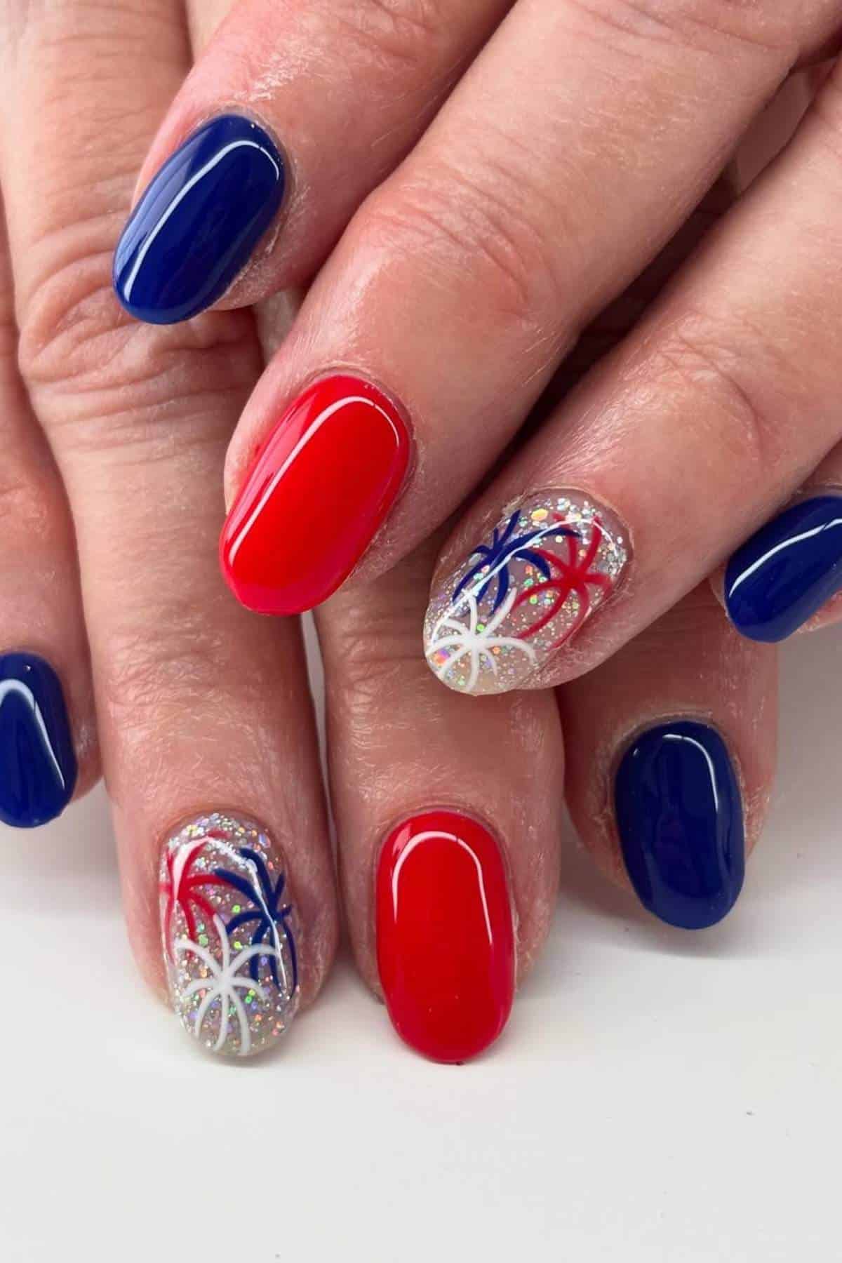 Hands with red, white, and blue nails. Two nails feature a firework design on a glitter base.