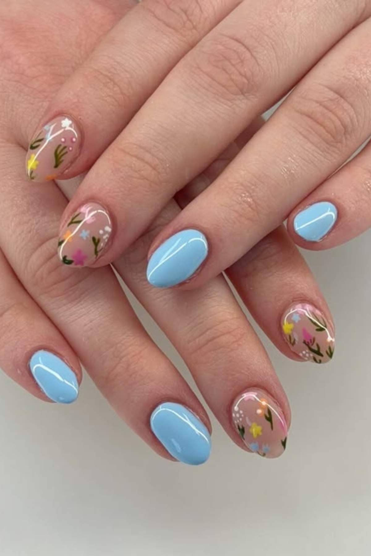 Hands with manicured nails; some nails are painted light blue, others are clear with small colorful floral designs.
