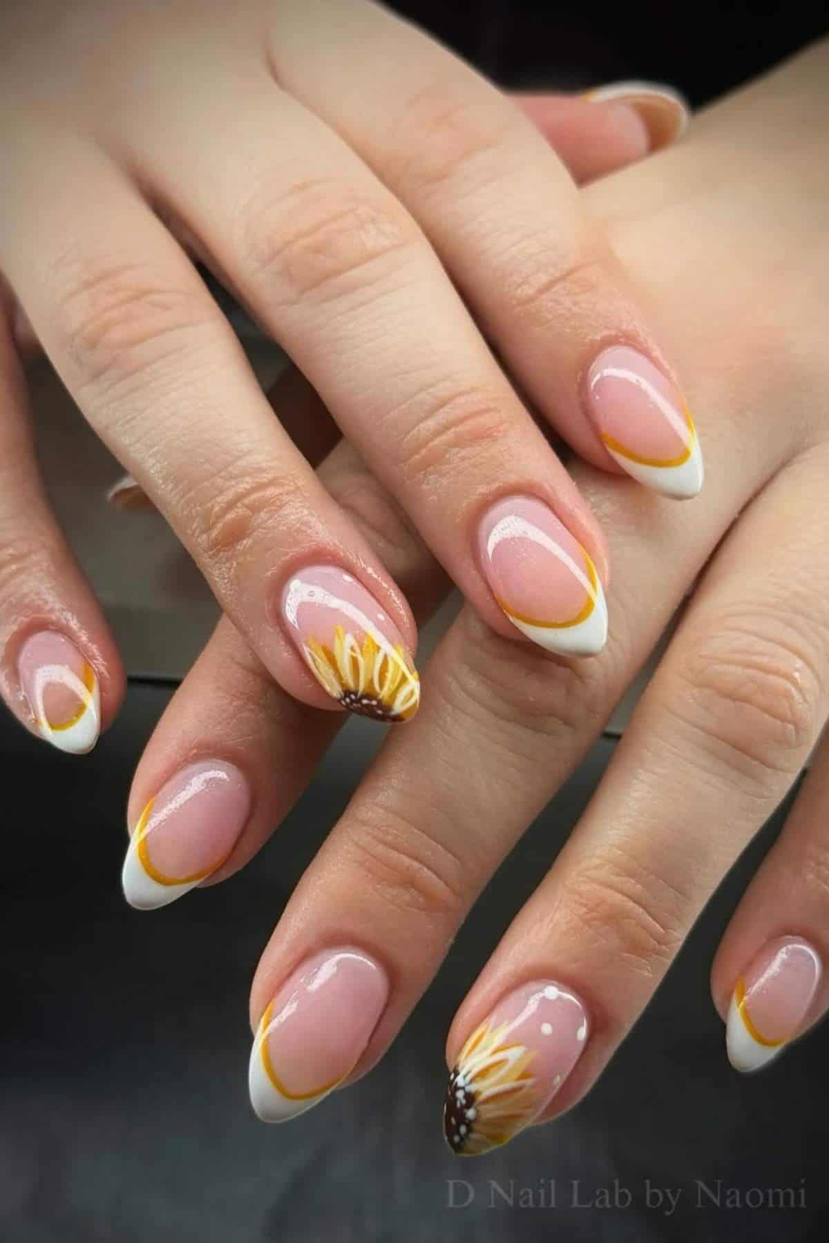 Hands with almond-shaped nails featuring a French manicure with yellow tips and sunflower designs on two accent nails.