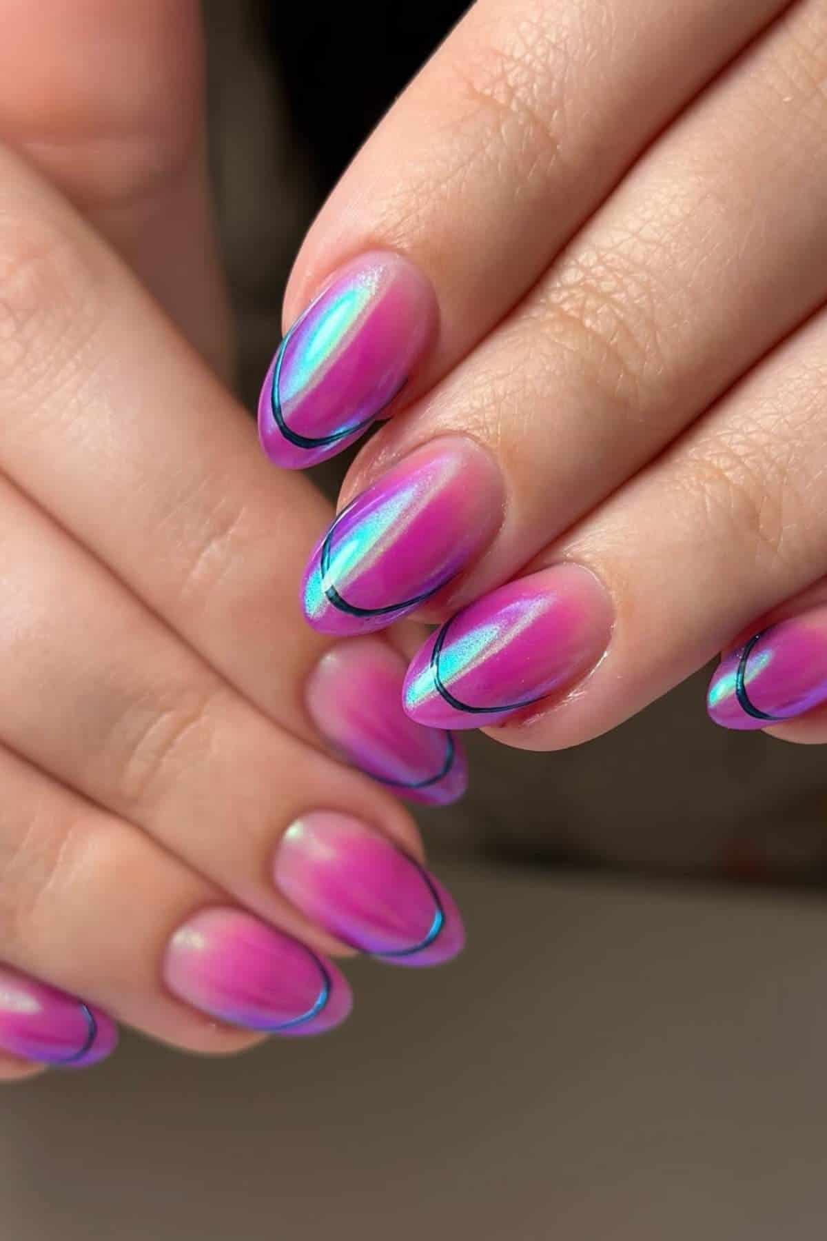 Close-up of hands with almond-shaped nails painted in a pink and purple iridescent design, featuring thin black curved lines near the tips.
