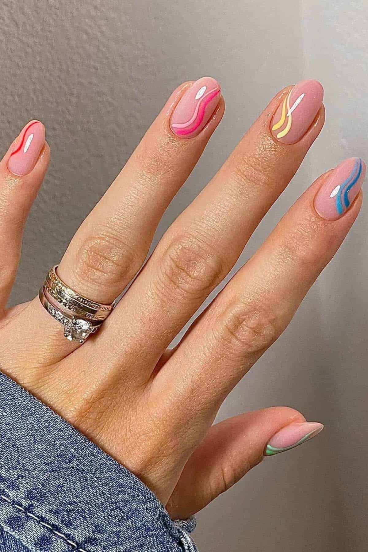 A hand with colorful abstract wavy nail art on almond-shaped nails, wearing three silver rings, against a light background.