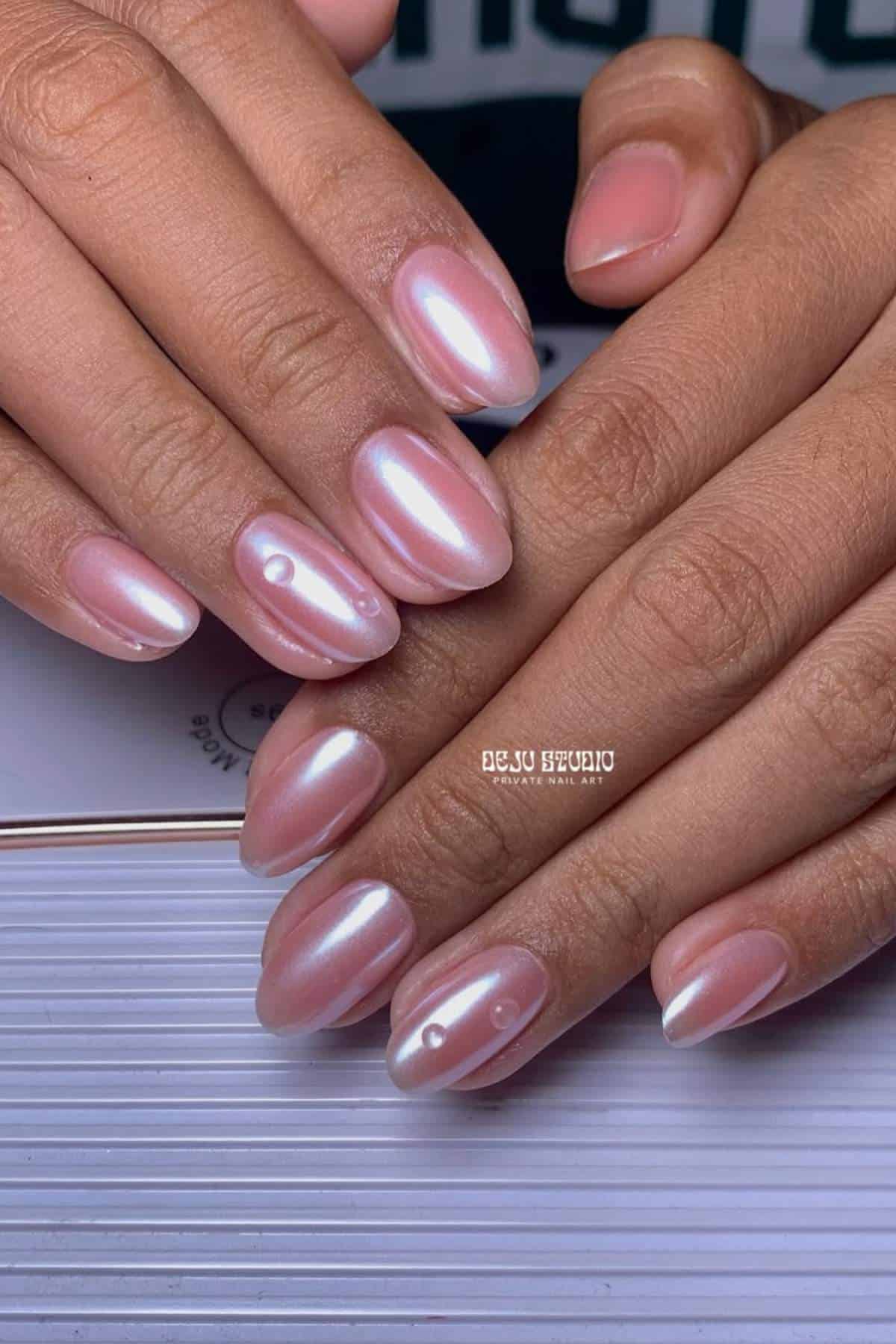 Hands with pearly pink almond-shaped nails, featuring a glossy finish and decorative droplets on two nails.