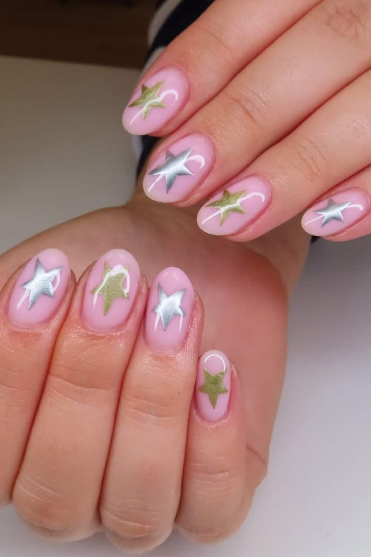 Close-up of hands with pink nail polish featuring metallic silver and gold star designs on each fingernail.
