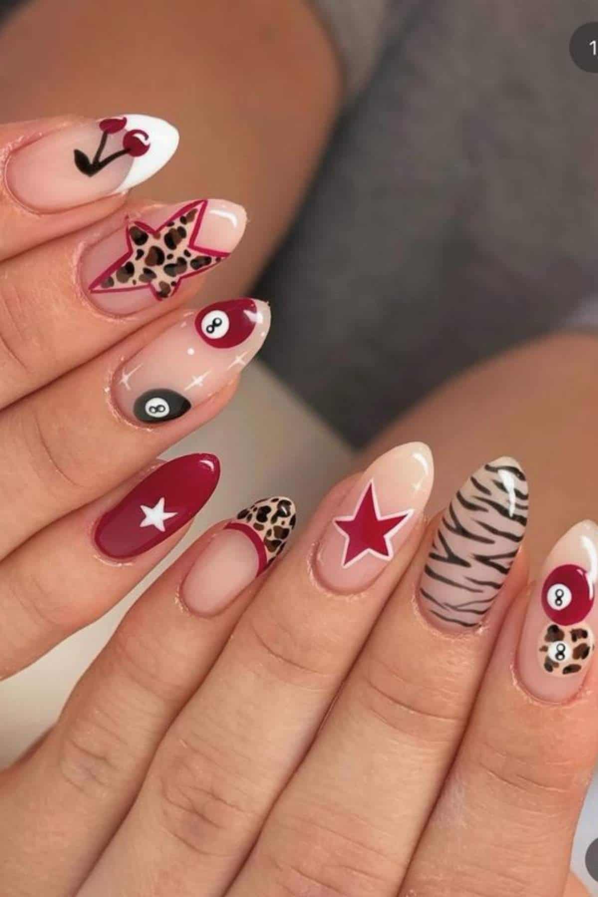 Hands with long, almond-shaped nails featuring various designs, including stars, cherries, leopard print, zebra stripes, and 8-ball patterns in red, black, and nude tones.