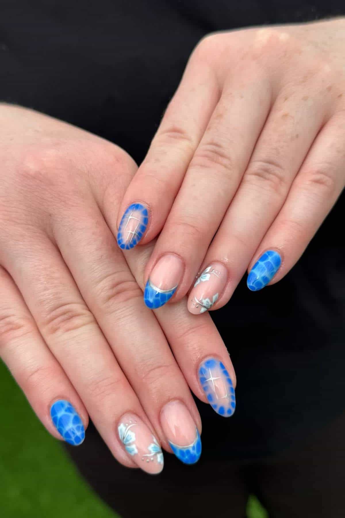 Close-up of hands with manicured nails featuring blue tips with a web design and accent nails with white floral patterns.