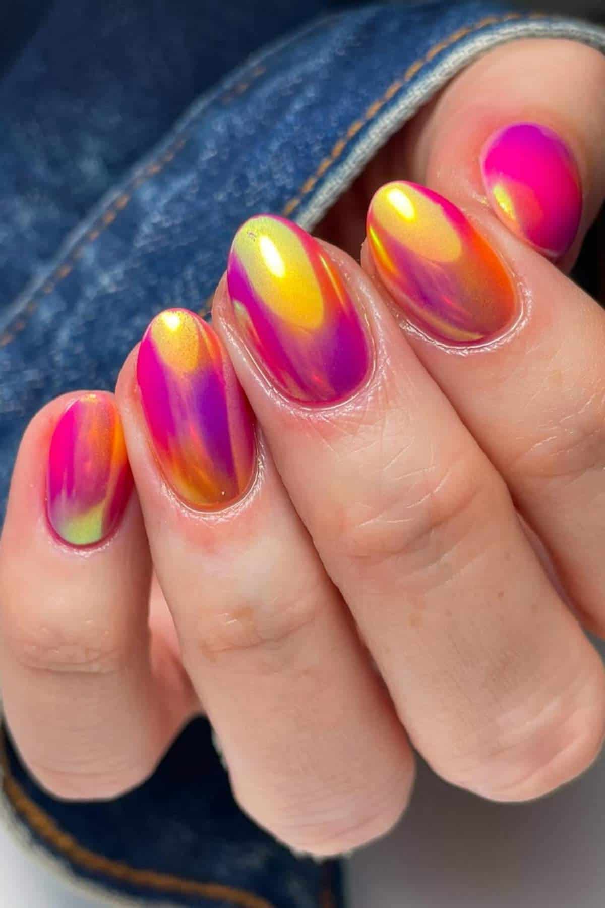 Close-up of a hand with short, oval-shaped nails featuring a colorful, iridescent gradient design in shades of pink, orange, yellow, and green.