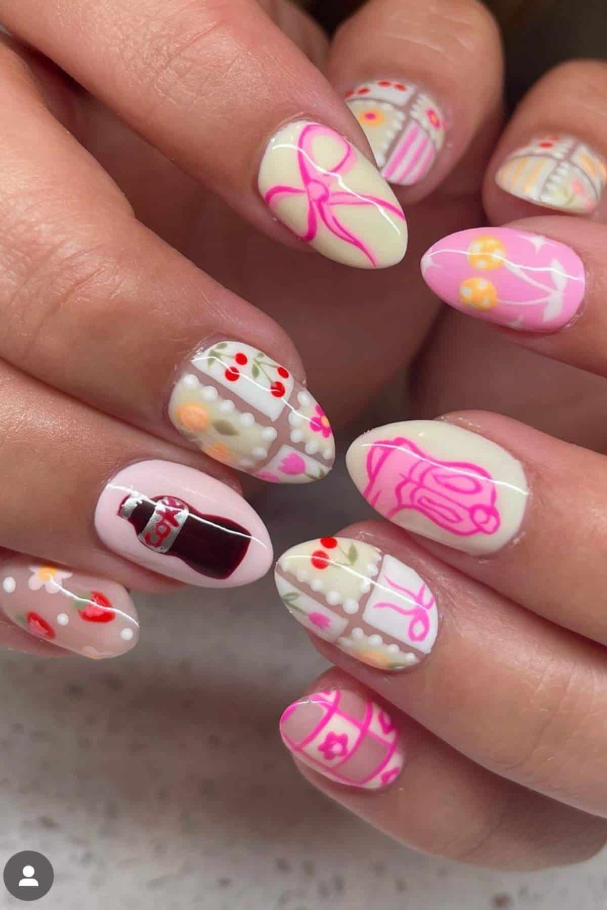 Close-up of hands with long almond-shaped nails featuring pastel nail art designs including bows, flowers, strawberries, and a bottle on a neutral background.