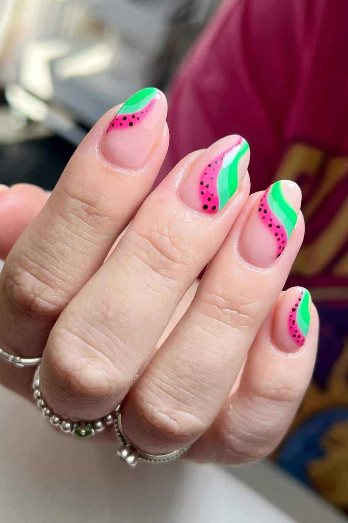 A hand with manicured nails painted in a watermelon-inspired design with pink, green, and black accents.