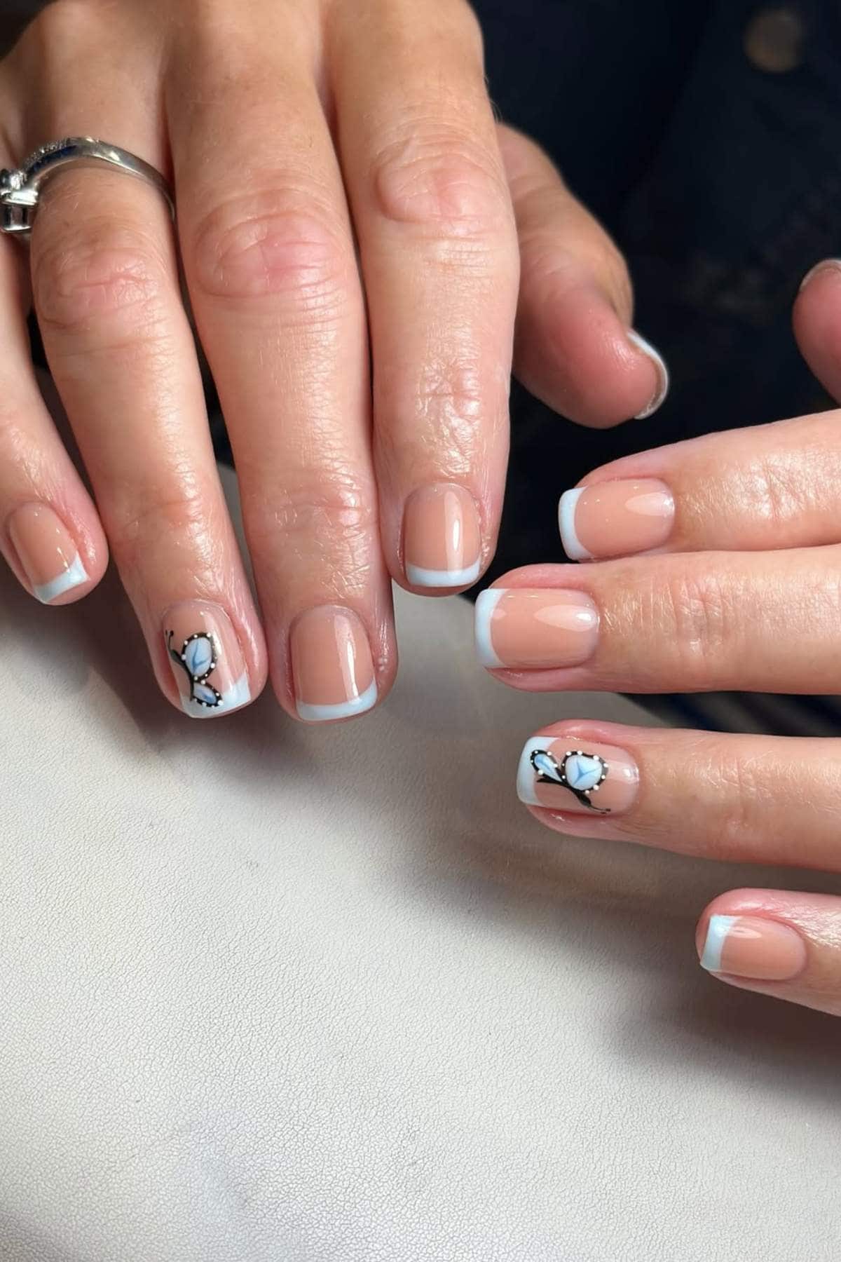 Hands with short, square-shaped French manicure; two nails feature a delicate black and white floral design.